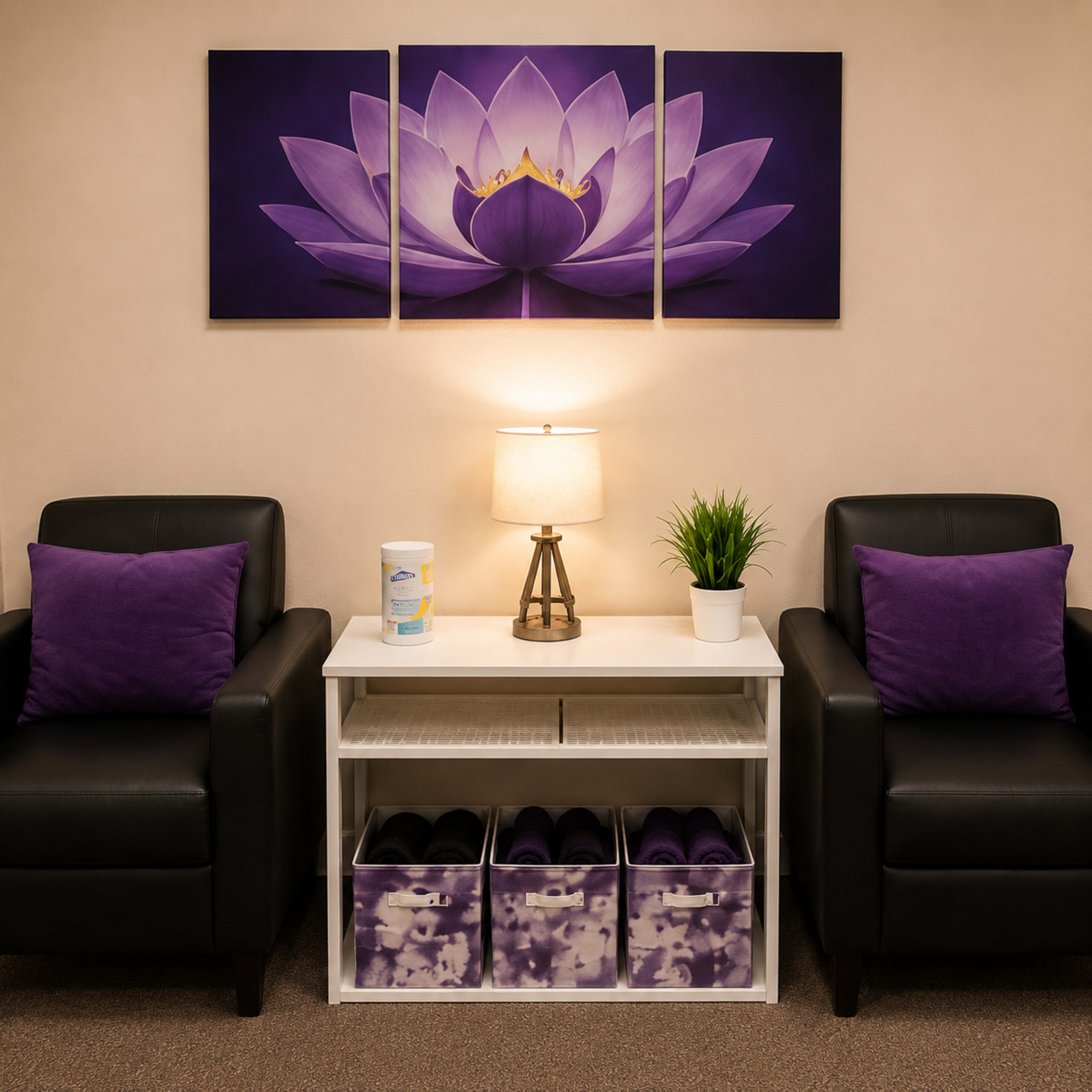 The image shows a calm waiting area with two black chairs adorned with purple pillows, a white table holding a lamp and a plant, and purple-themed storage boxes beneath.