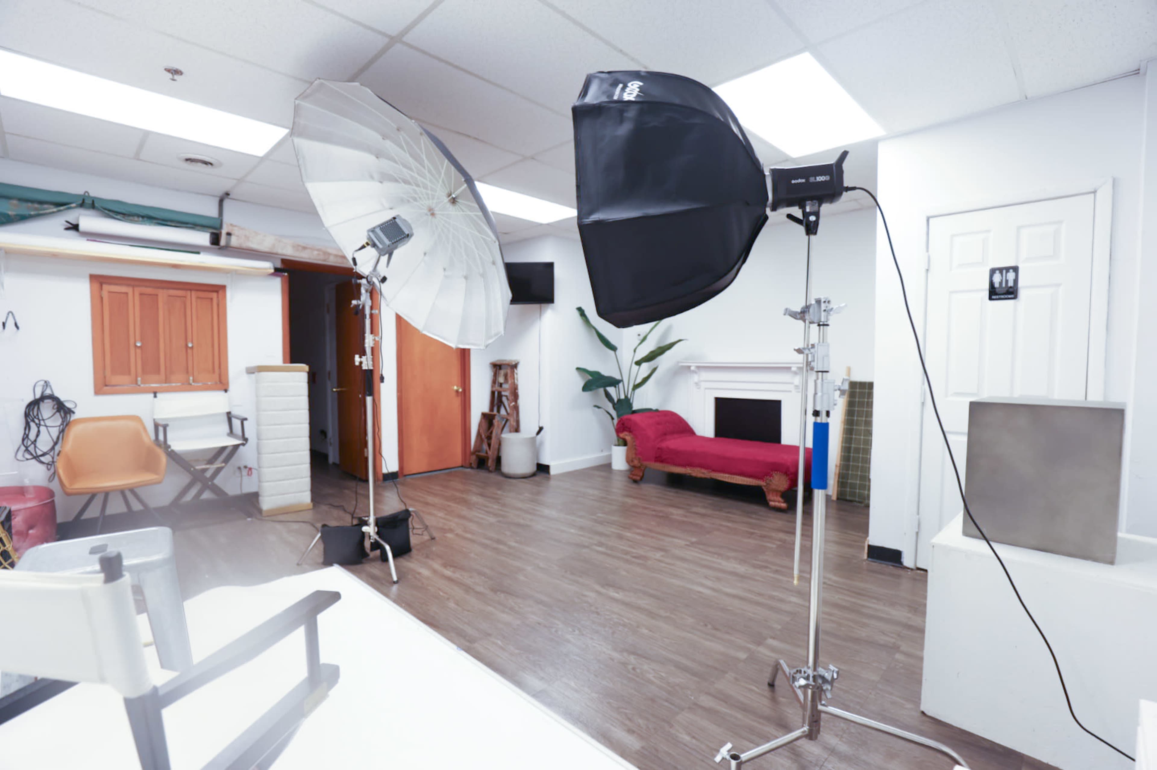 A photography studio with two lighting setups, a red couch, and various props in the background.