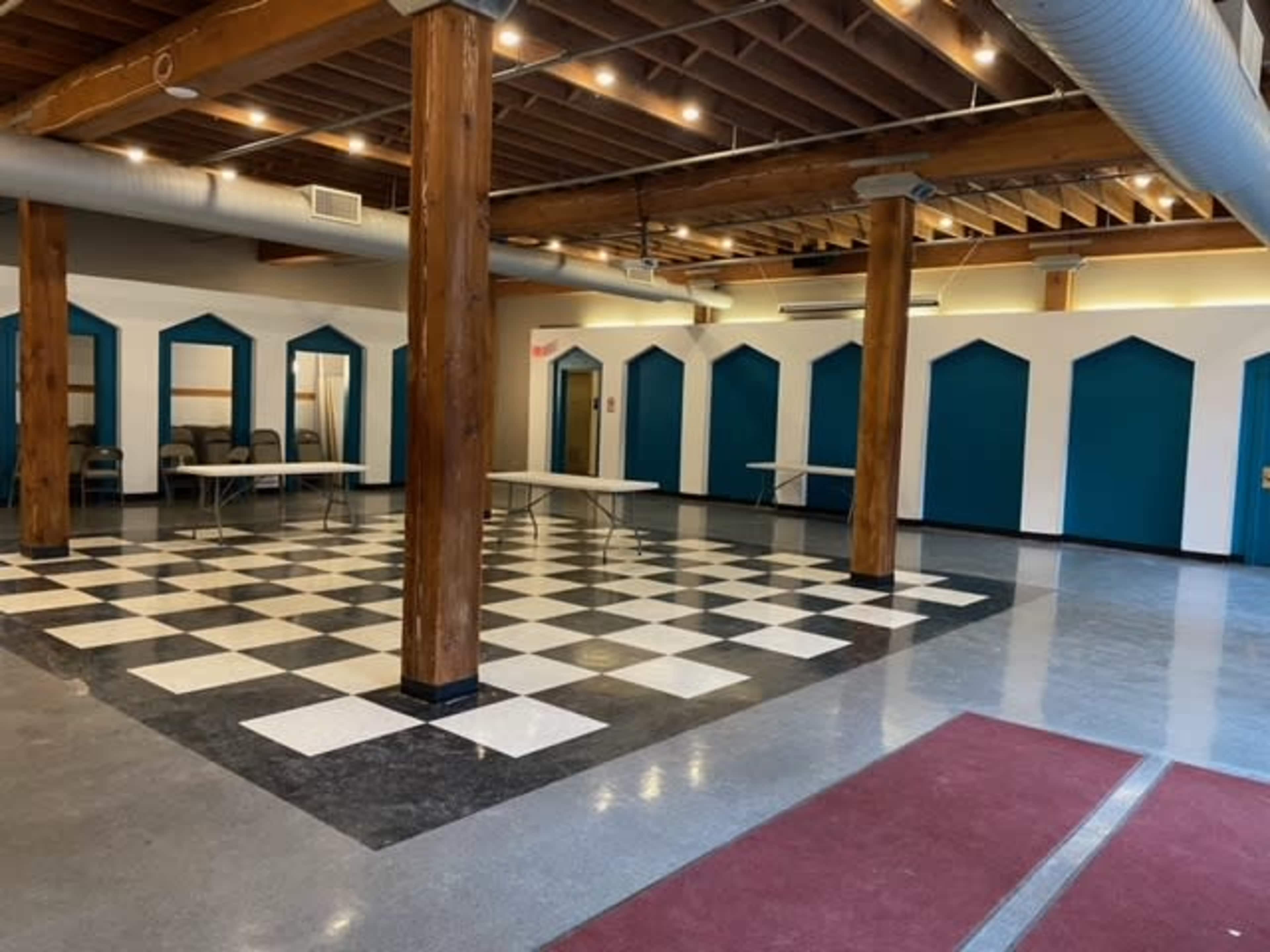 A large, open room with a checkered floor pattern, wooden columns, and blue-accented, arched wall sections.