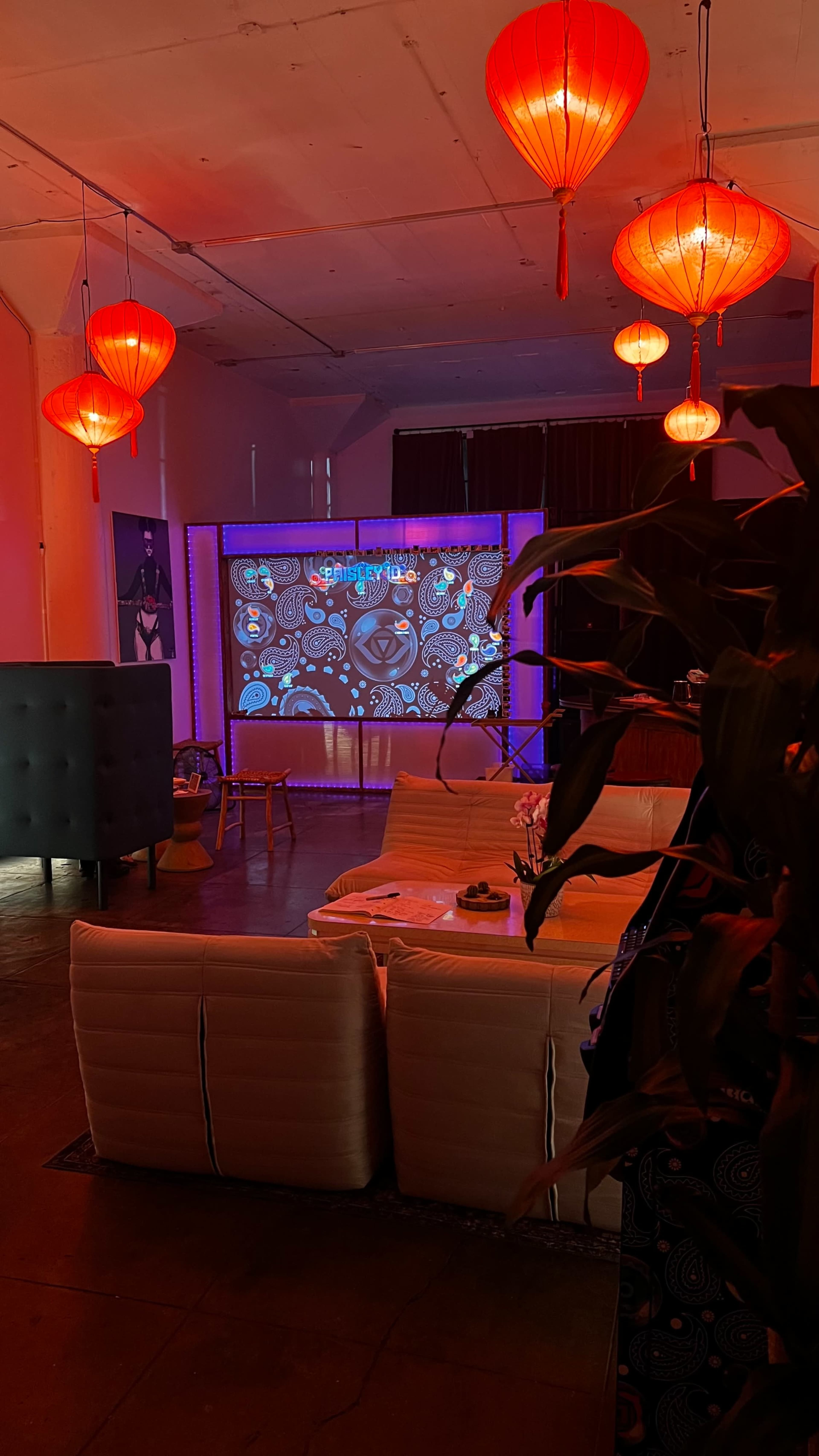 The image shows a brightly lit room with red lanterns, a projector displaying colorful patterns, and modern seating arrangements.