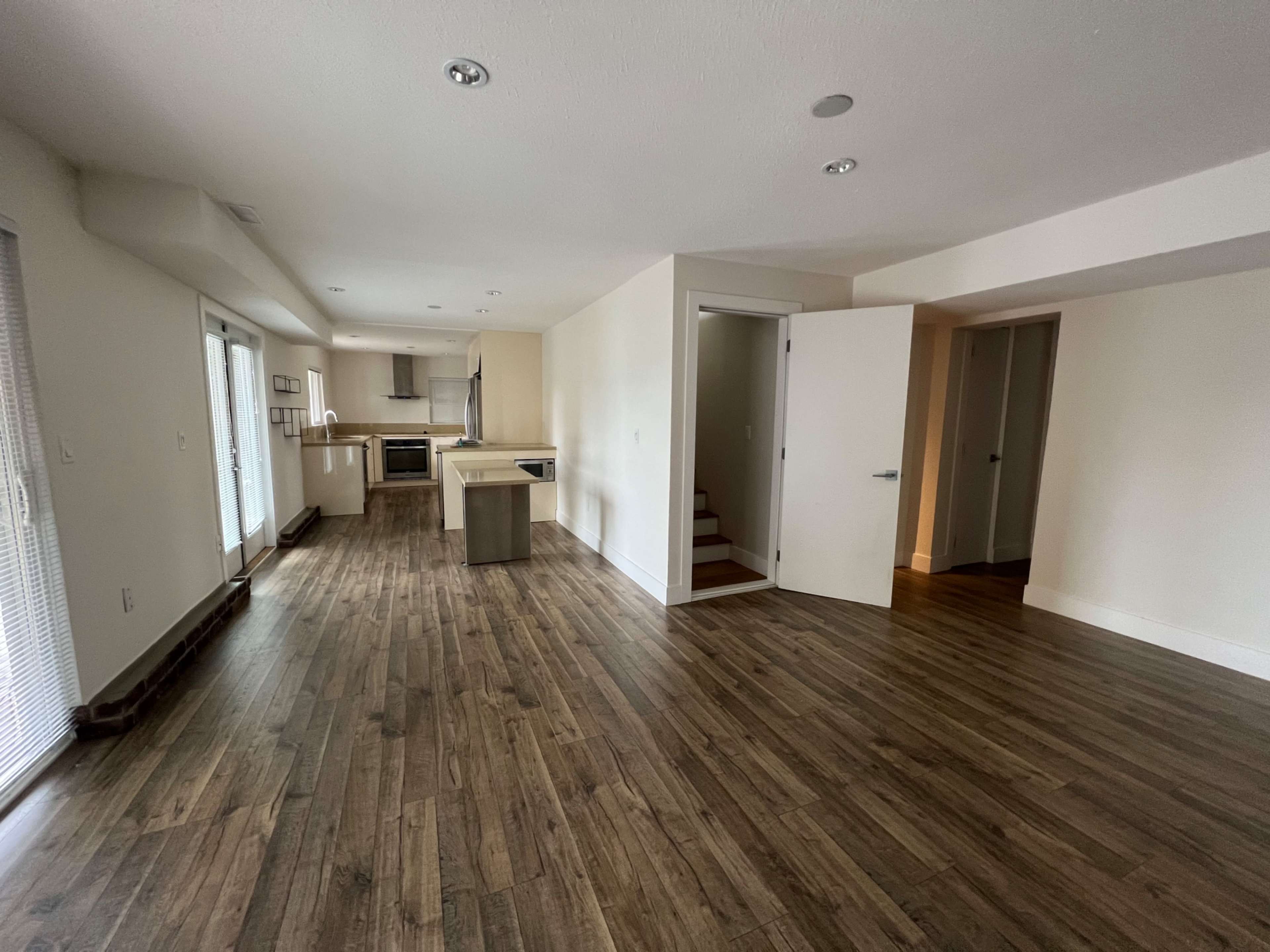An open-concept living space with hardwood flooring, a kitchen area, and a staircase leading to a second level.