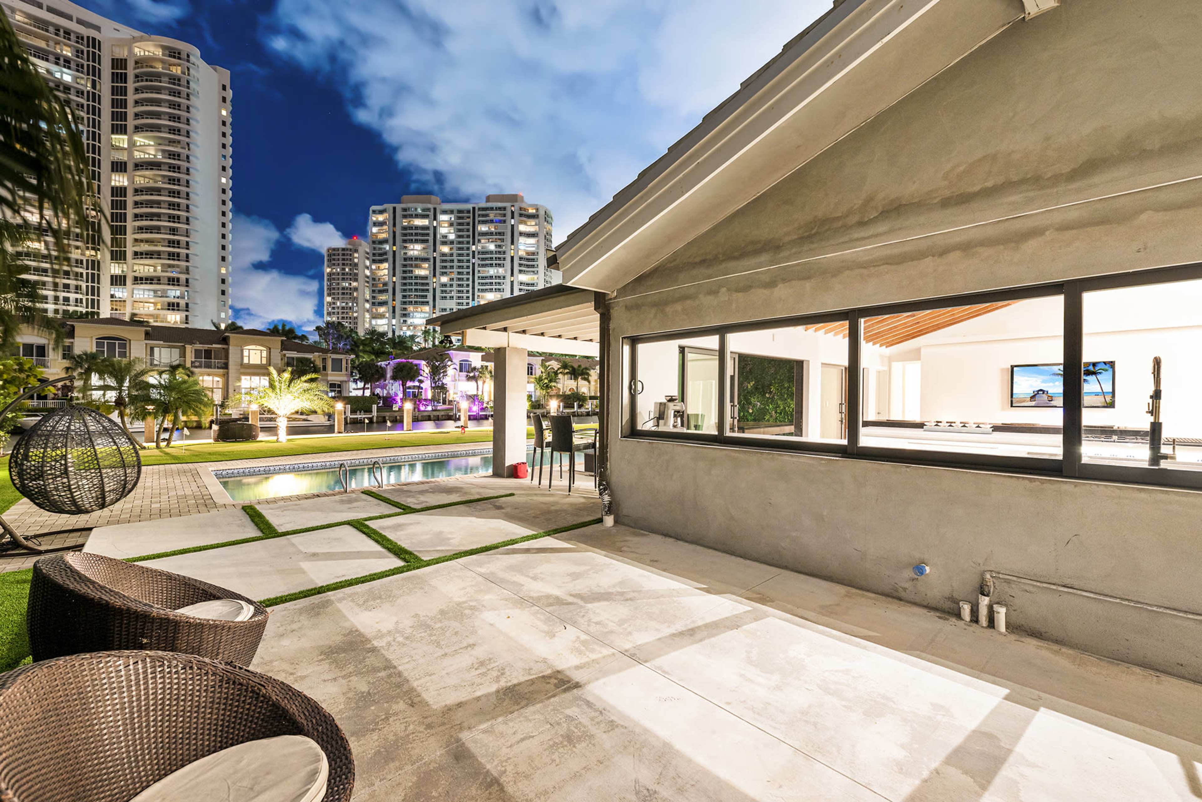 A modern outdoor patio area with a swimming pool, surrounded by residential buildings and illuminated by evening lights.