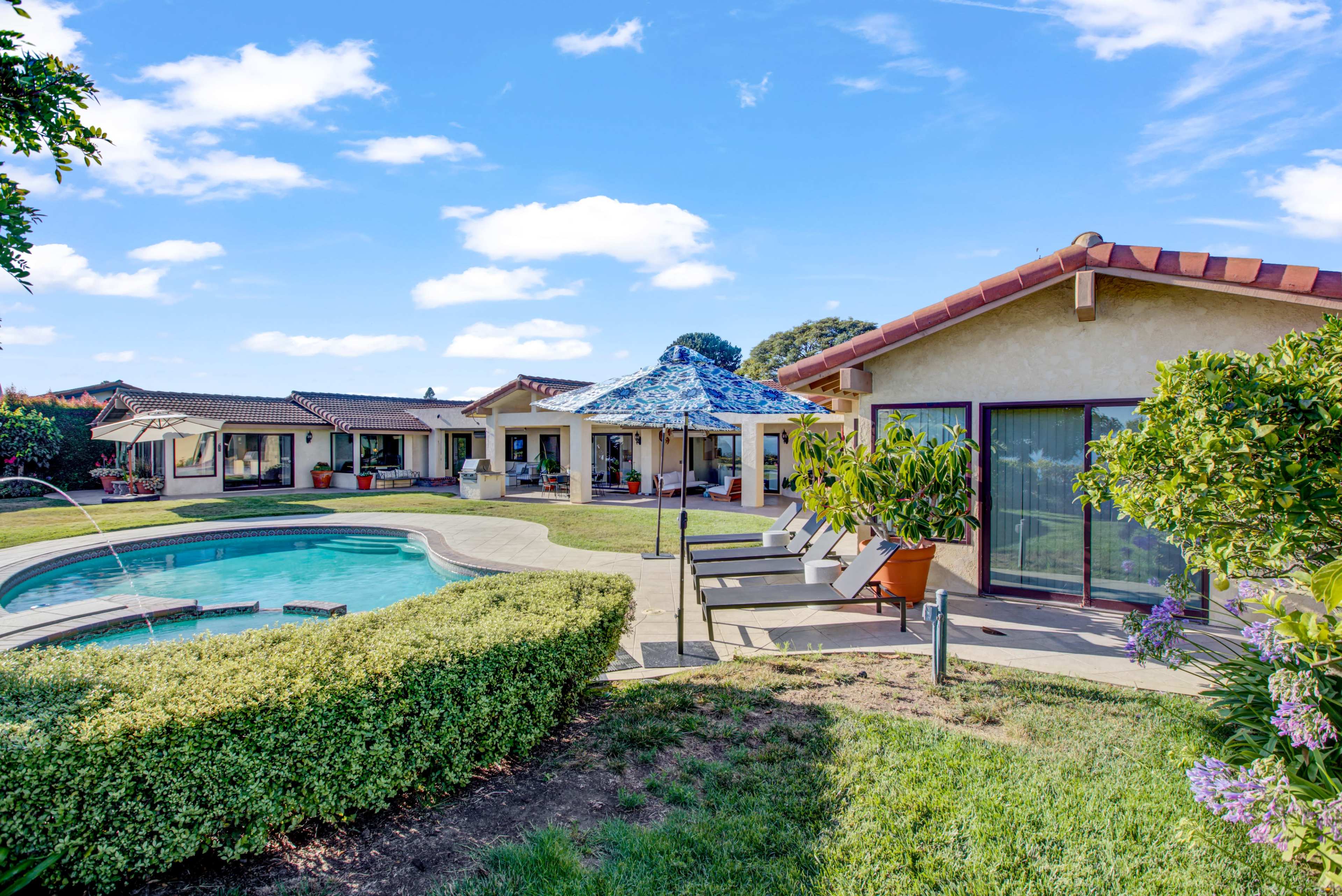A residential property featuring a swimming pool, landscaped lawn, and multiple single-story buildings under a clear blue sky.