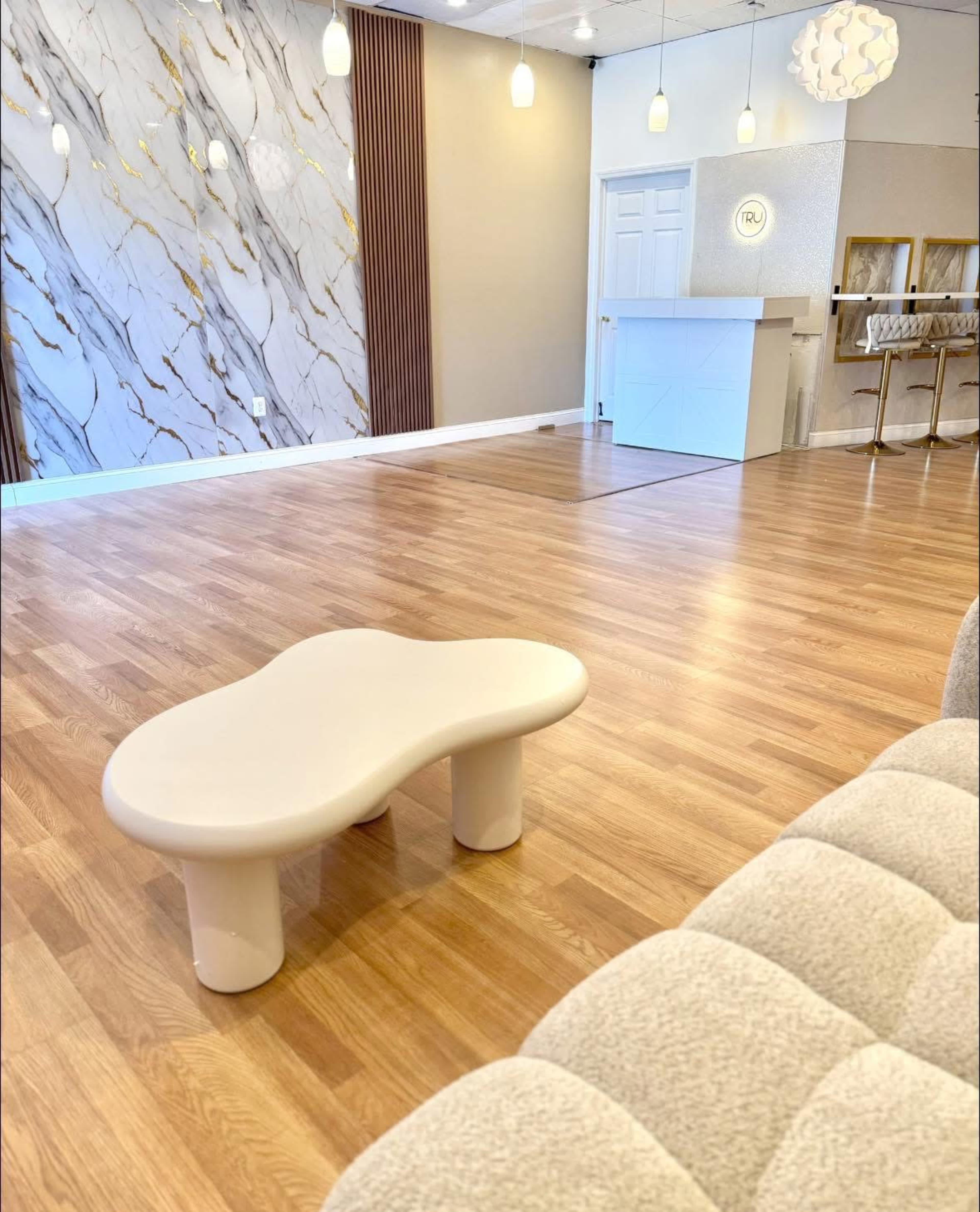 The image shows a spacious room featuring a modern light-colored table in the center, a textured wall with marble patterns, and various light fixtures above.