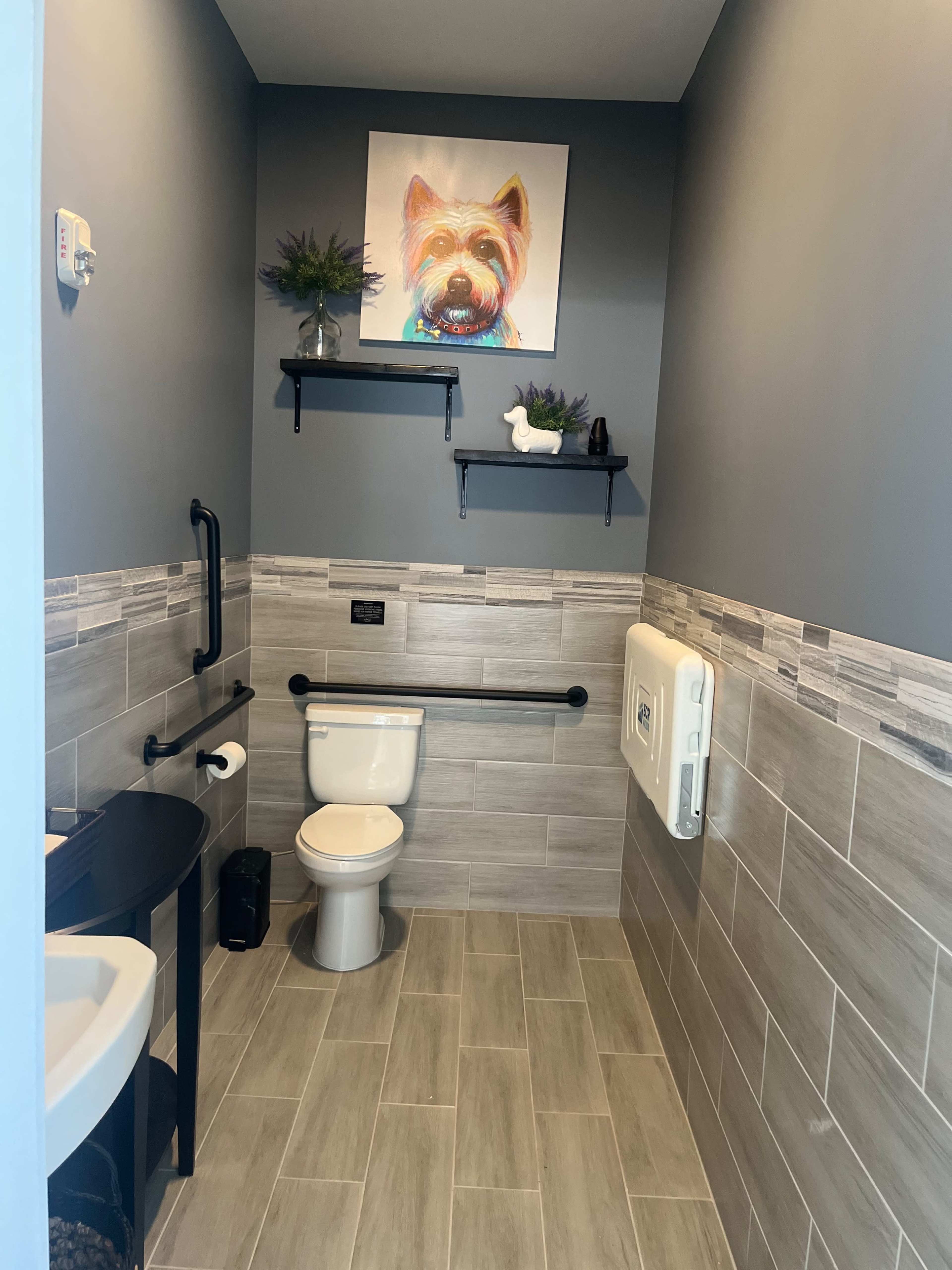 The image shows a small bathroom with a toilet, a sink, and two shelves featuring decor on the walls.