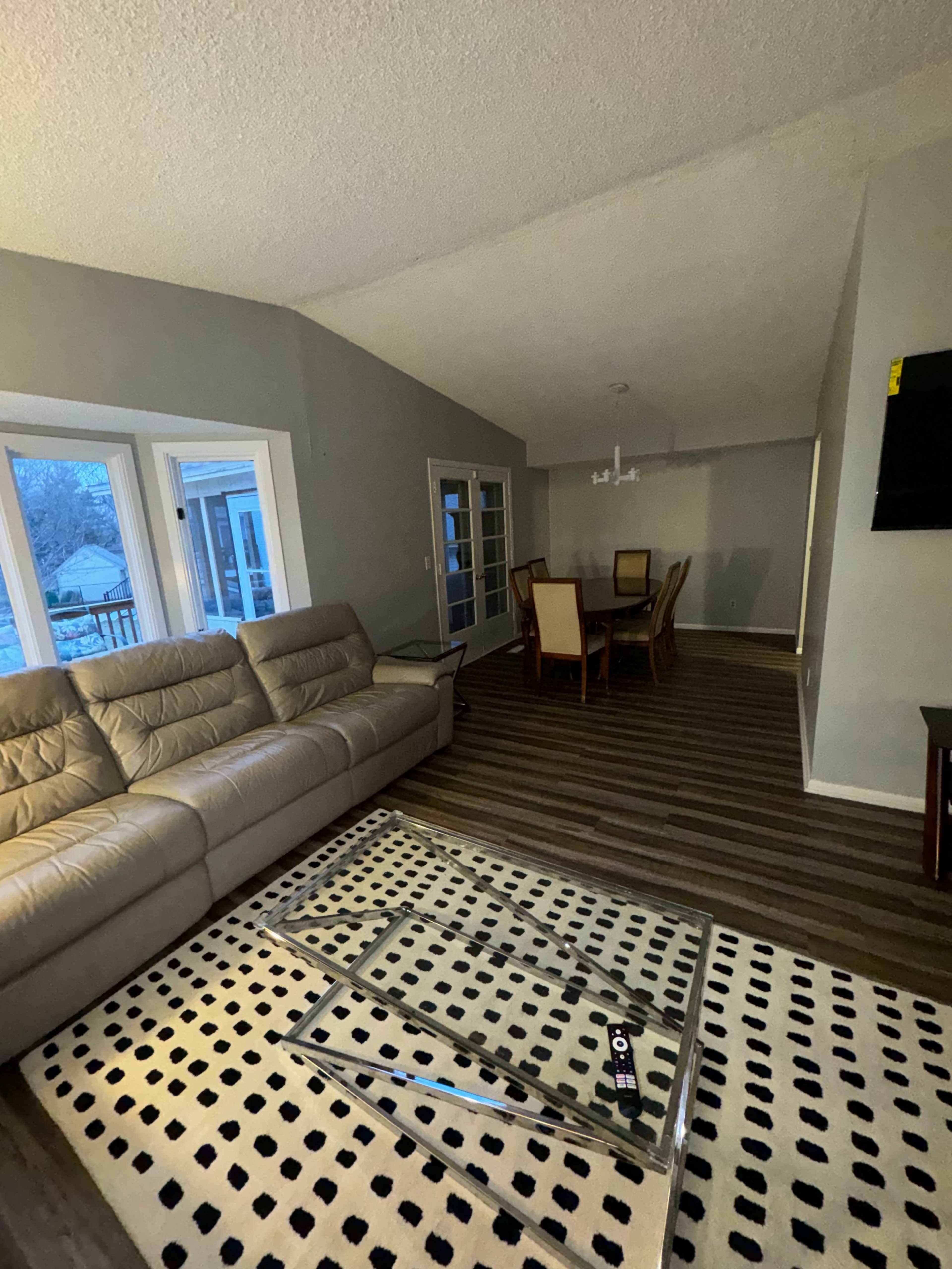 A living room with a beige sectional sofa, a glass coffee table, and a dining area with a wooden table and chairs.