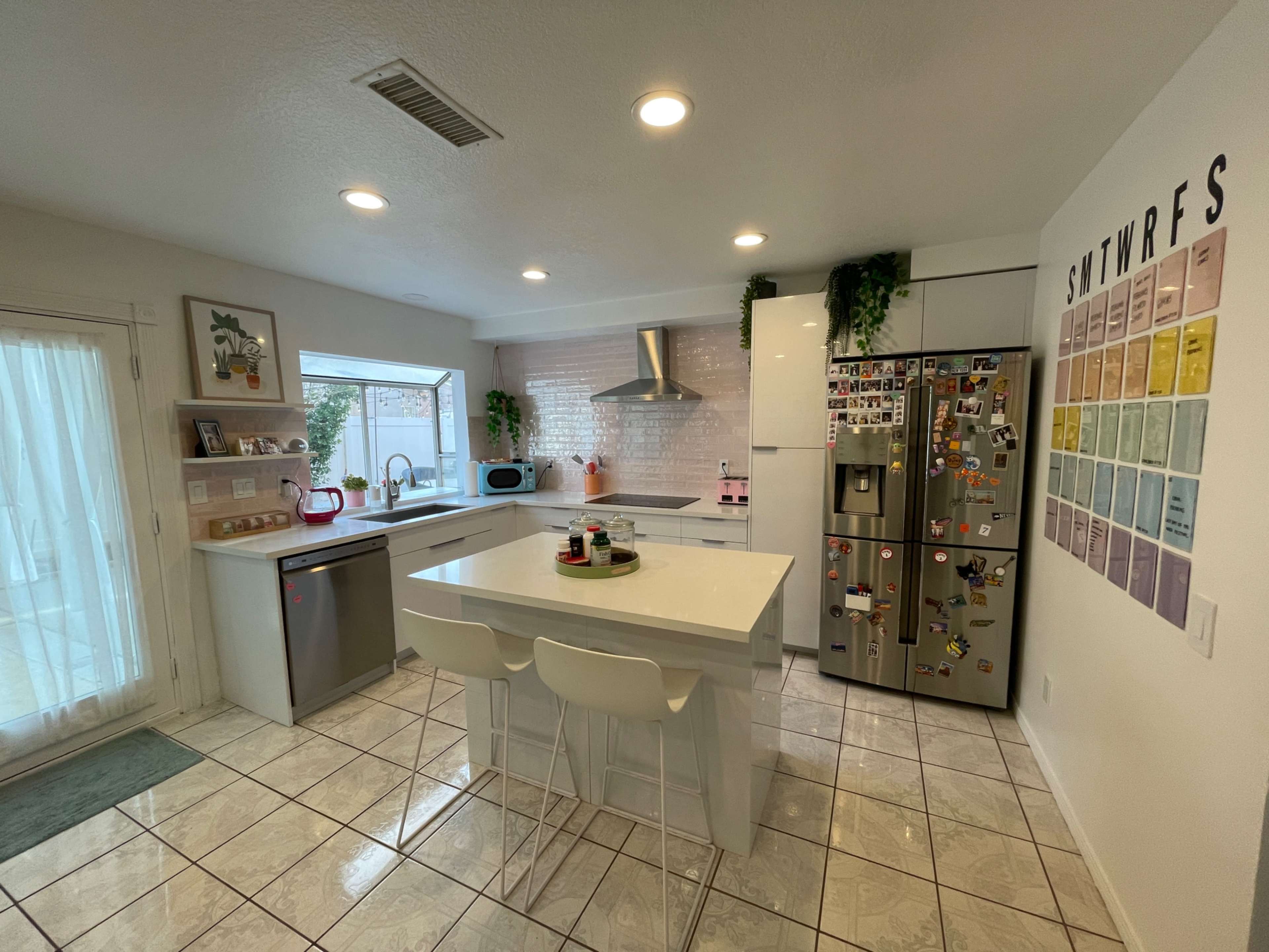 A modern kitchen featuring a central island with stools, stainless steel appliances, and light-colored tiled flooring.