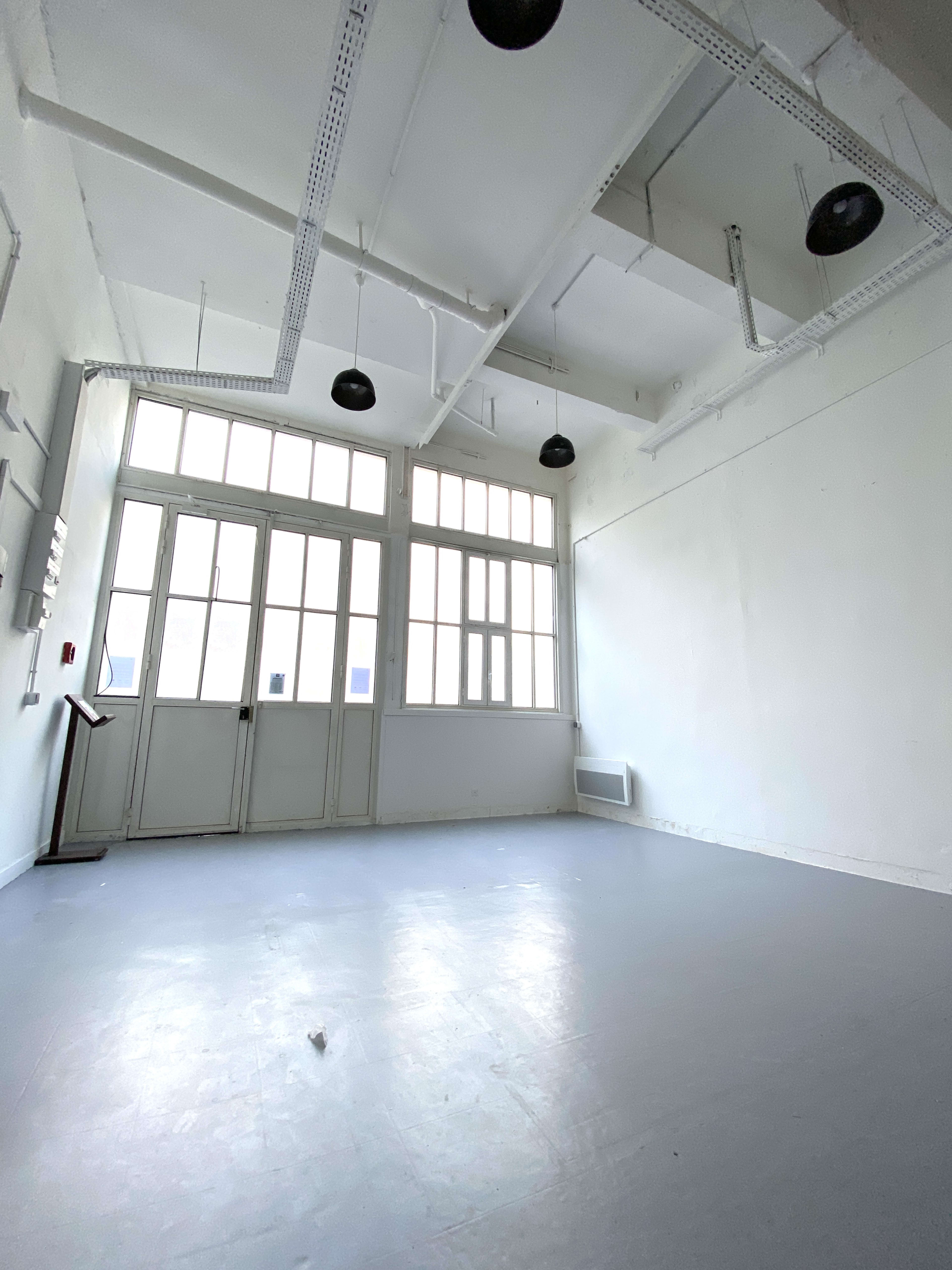 An empty room with high ceilings, large windows, and fluorescent lights.