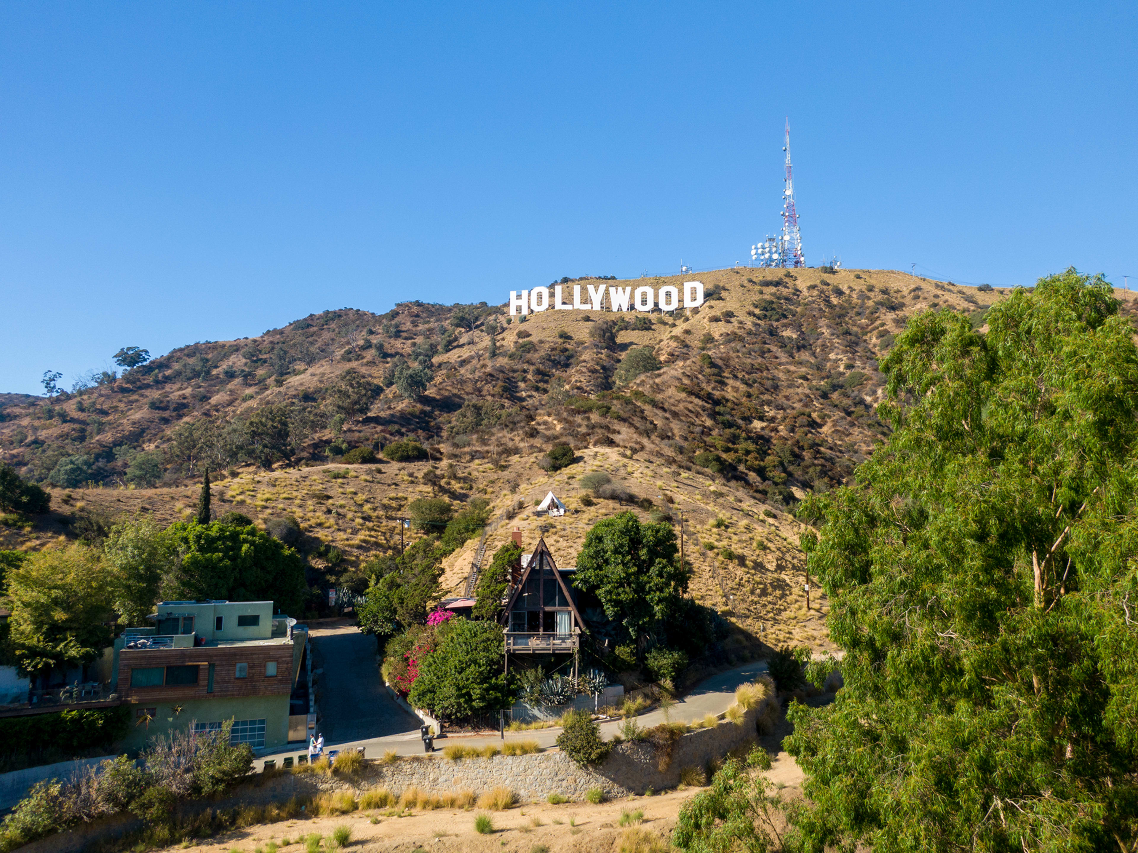 The iconic Hollywood sign is prominently displayed on a hillside, overlooking a cluster of buildings and trees below.