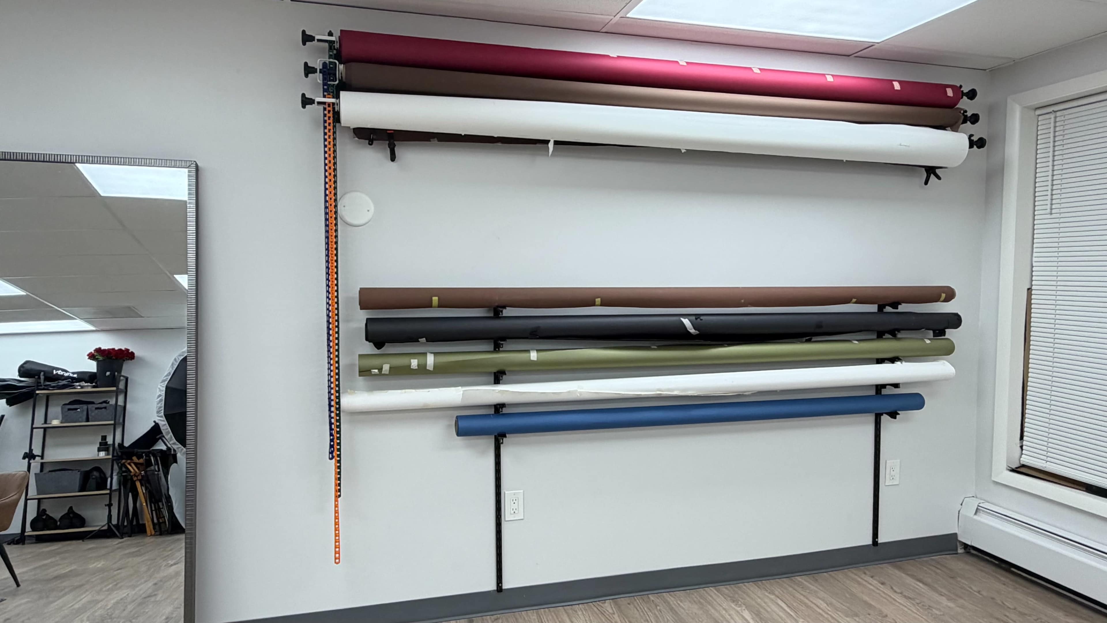 The image shows a wall displaying various rolls of backdrop paper in different colors, neatly organized on mounted poles.