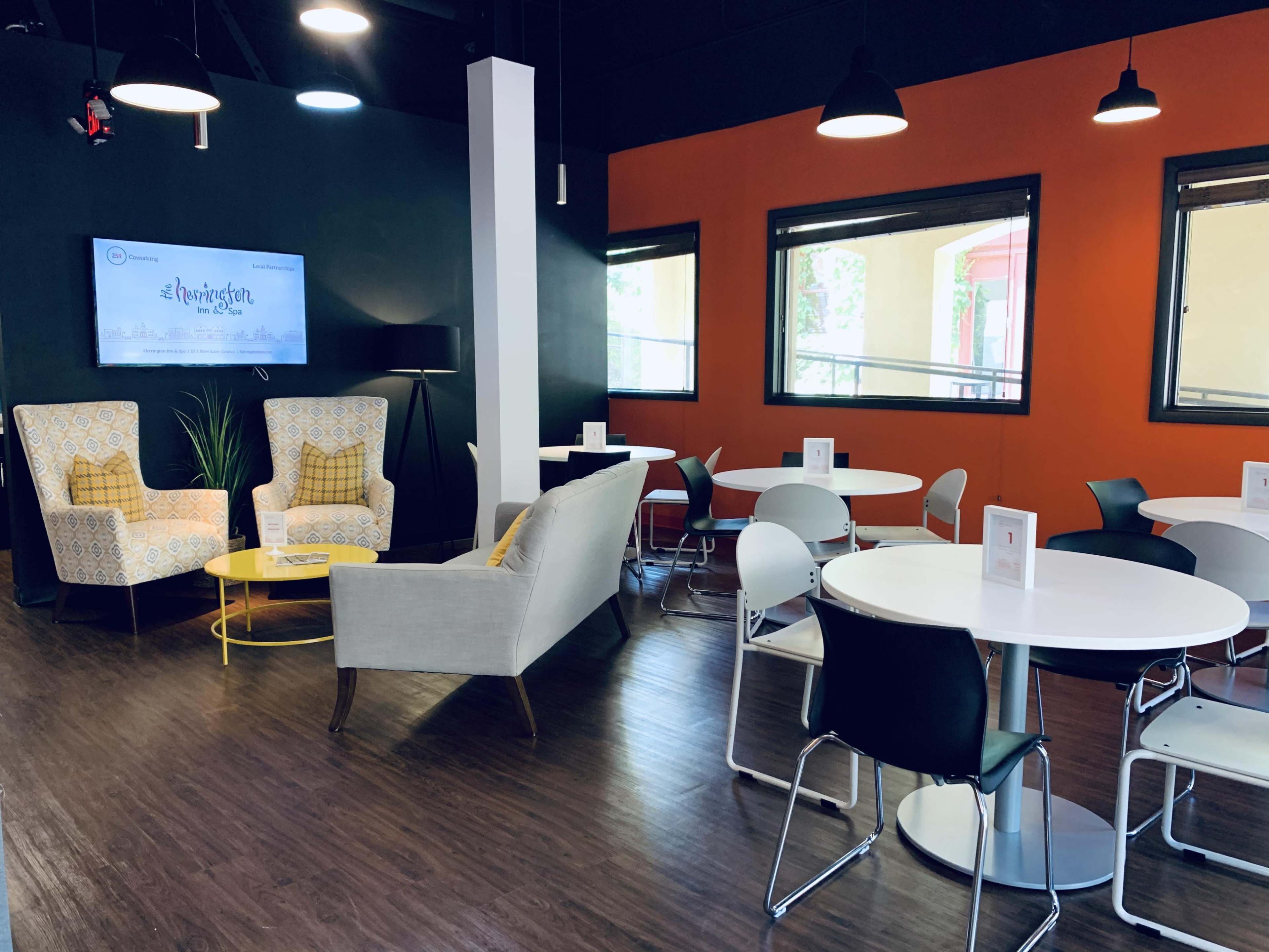 A modern lounge area with two patterned armchairs, a yellow side table, and several circular white tables with black and chrome chairs.