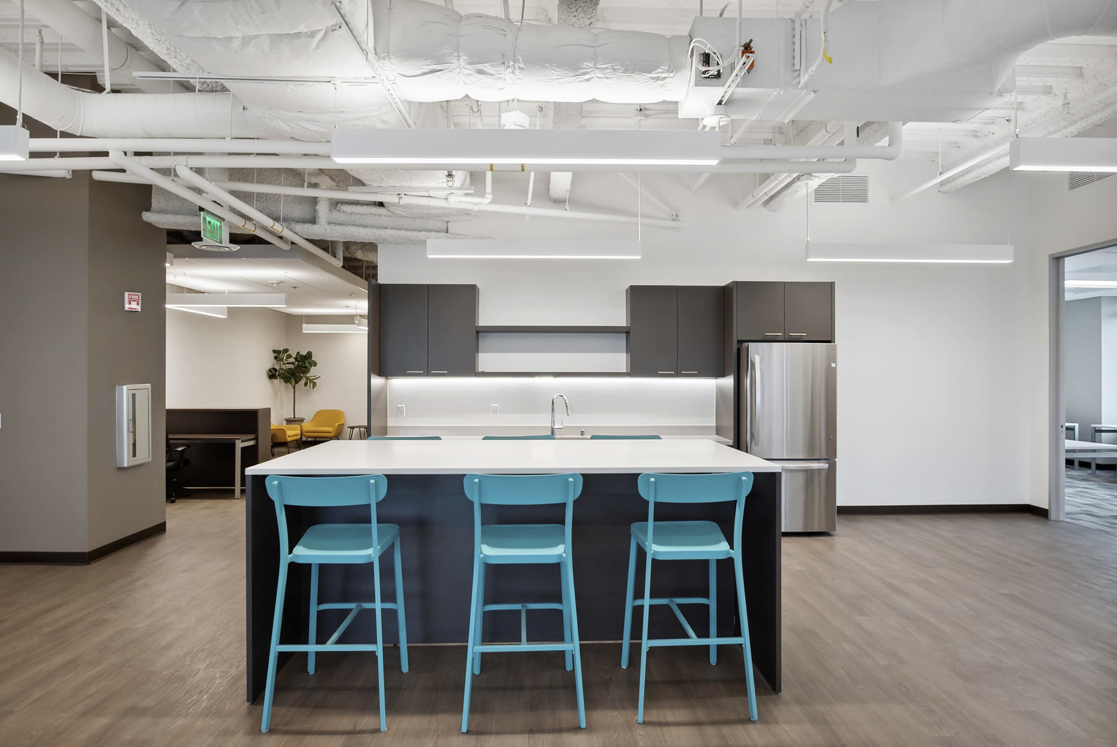 A modern kitchen area features a dark island with a light countertop and four blue stools.