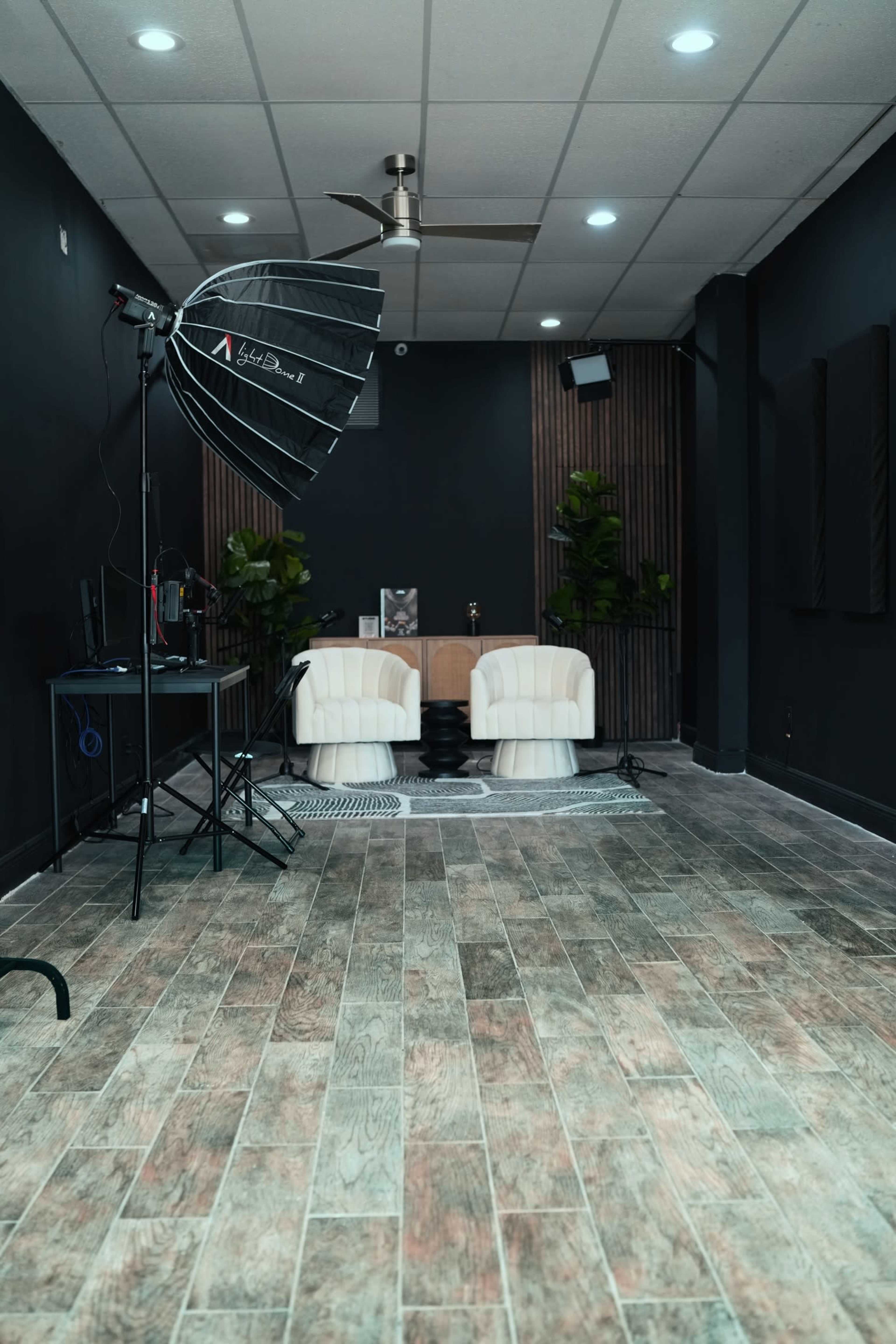 A photography studio featuring two white chairs, a backdrop, and studio lighting equipment against a dark wall.