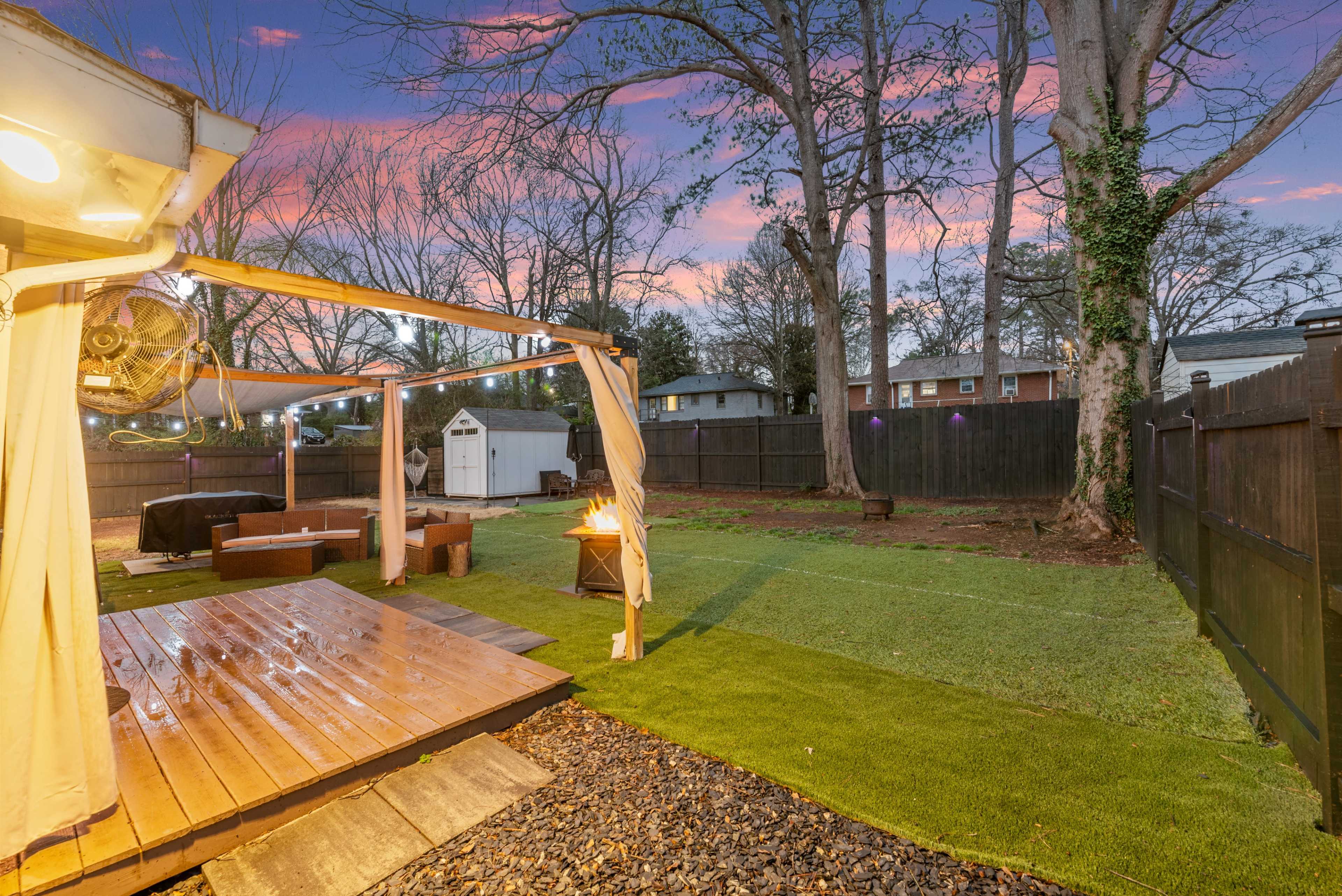 The image shows a backyard with a wooden deck, a grassy area, and a small shed in the background under a colorful sunset sky.