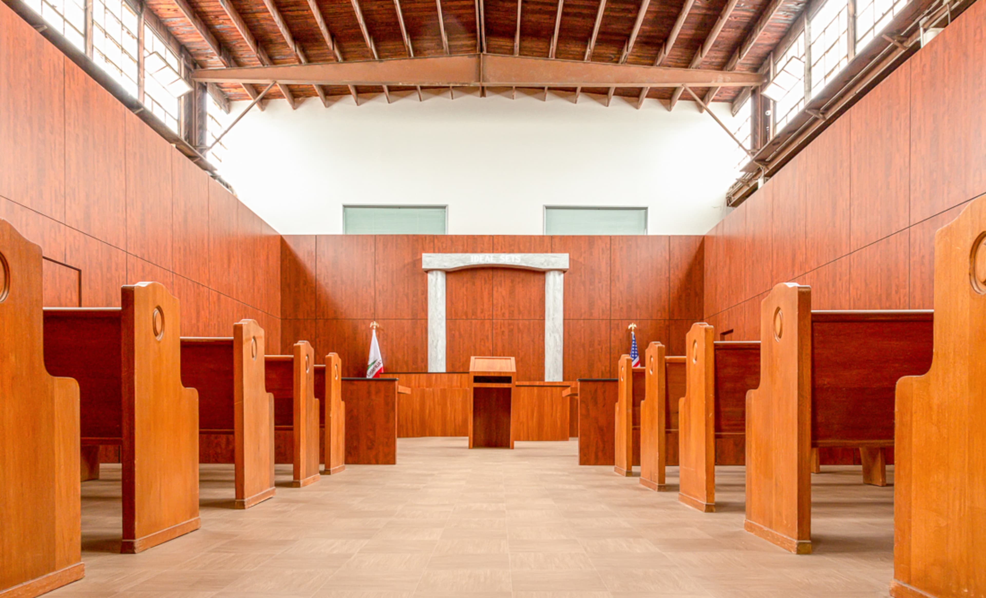 A courtroom with wooden seating, a central judge's bench, and flags positioned at the front.