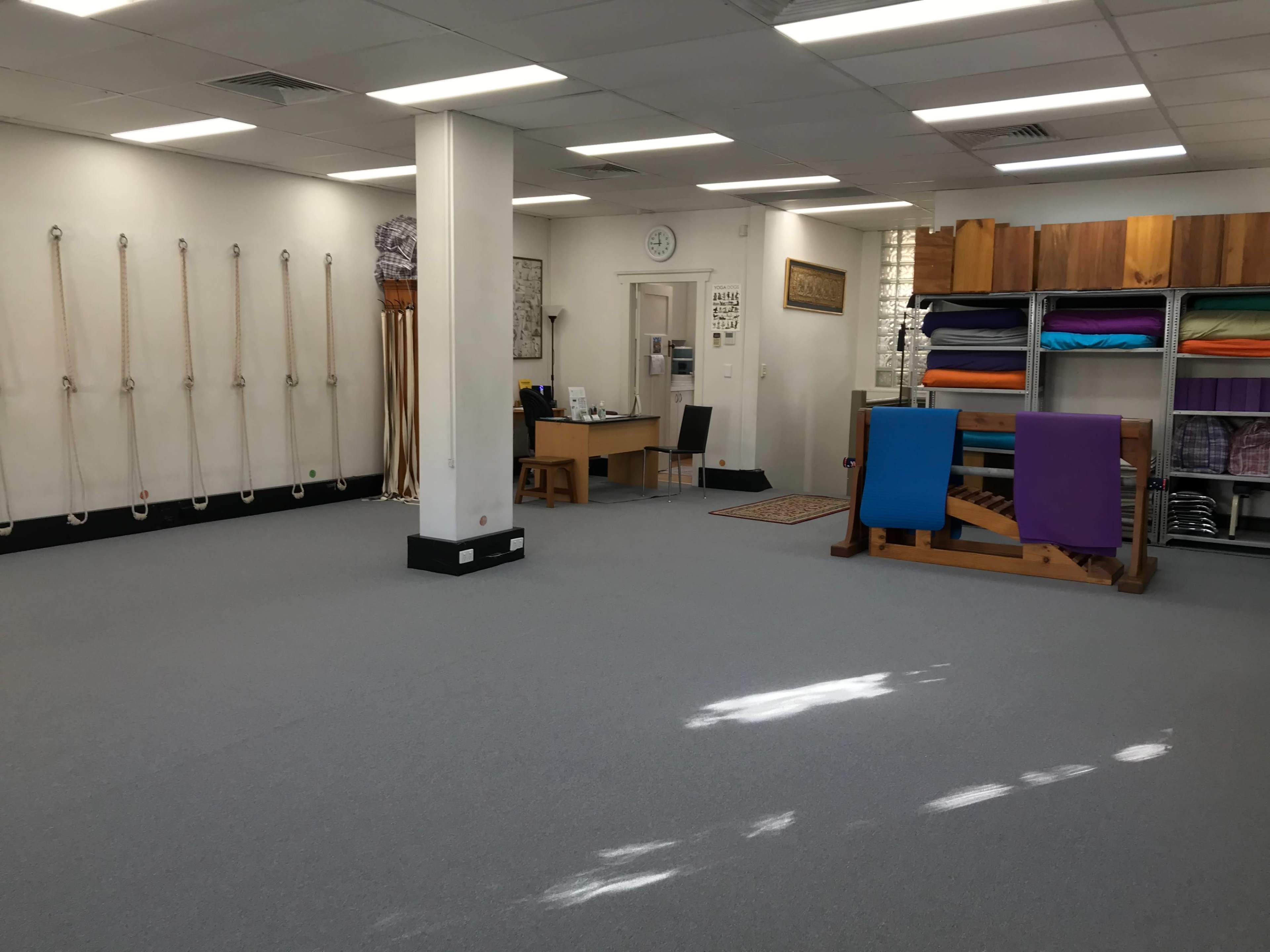 A spacious, well-lit studio with exercise ropes and colorful yoga mats neatly arranged on shelves.