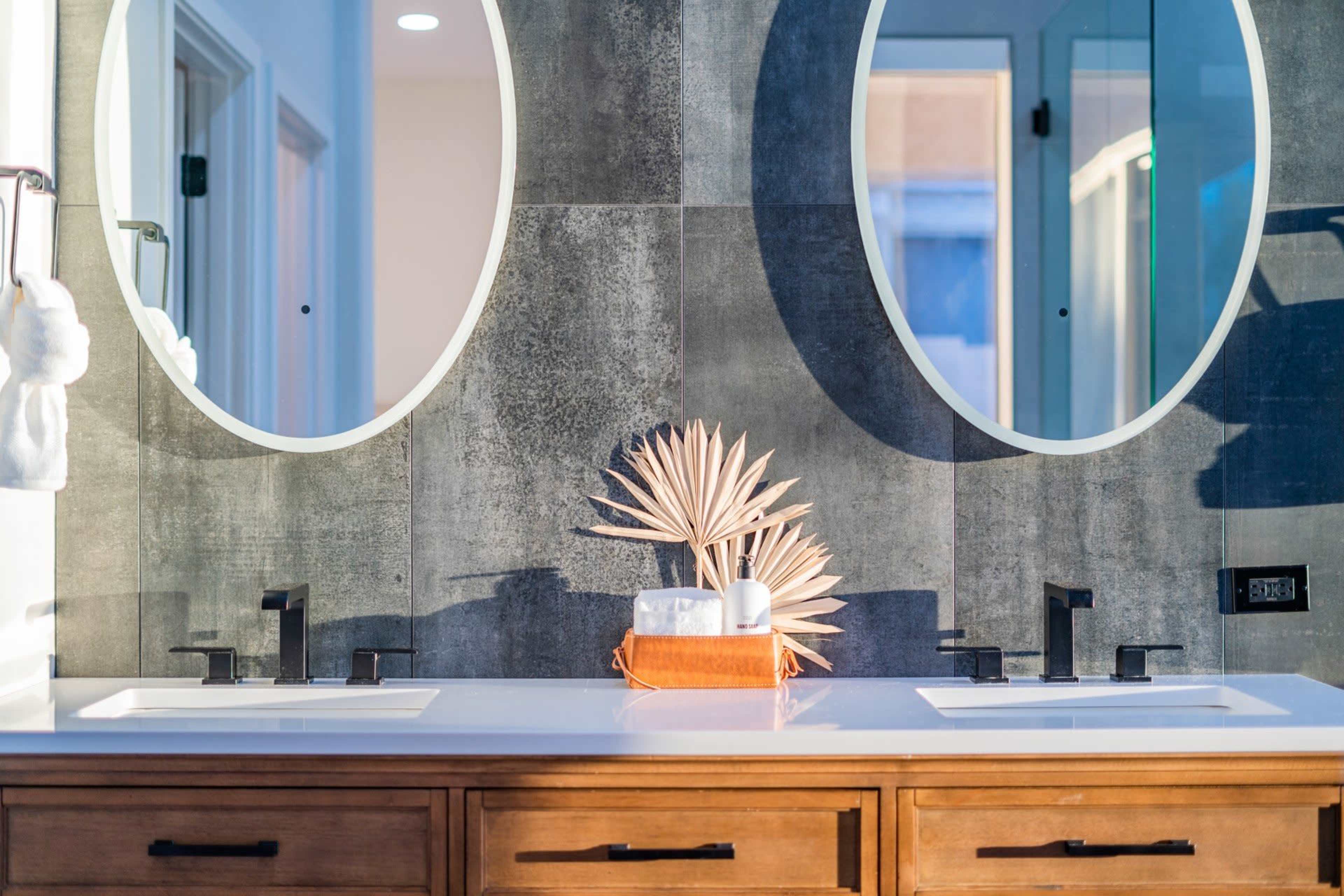 A bathroom vanity features two oval mirrors above a double sink with modern faucets, flanked by decorative elements on a wooden countertop.