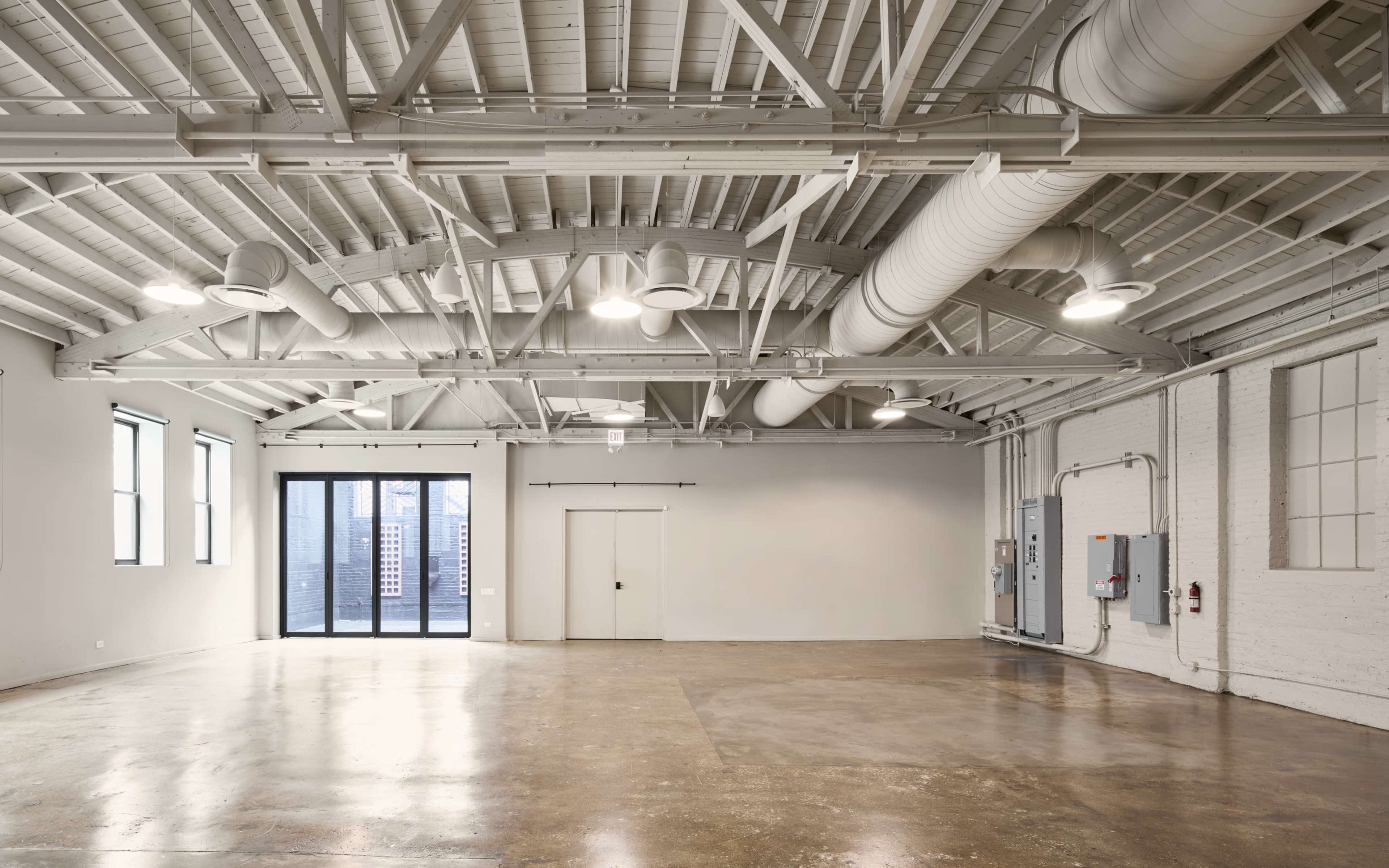The image shows a spacious, empty room with high ceilings, large windows, and polished concrete floors.