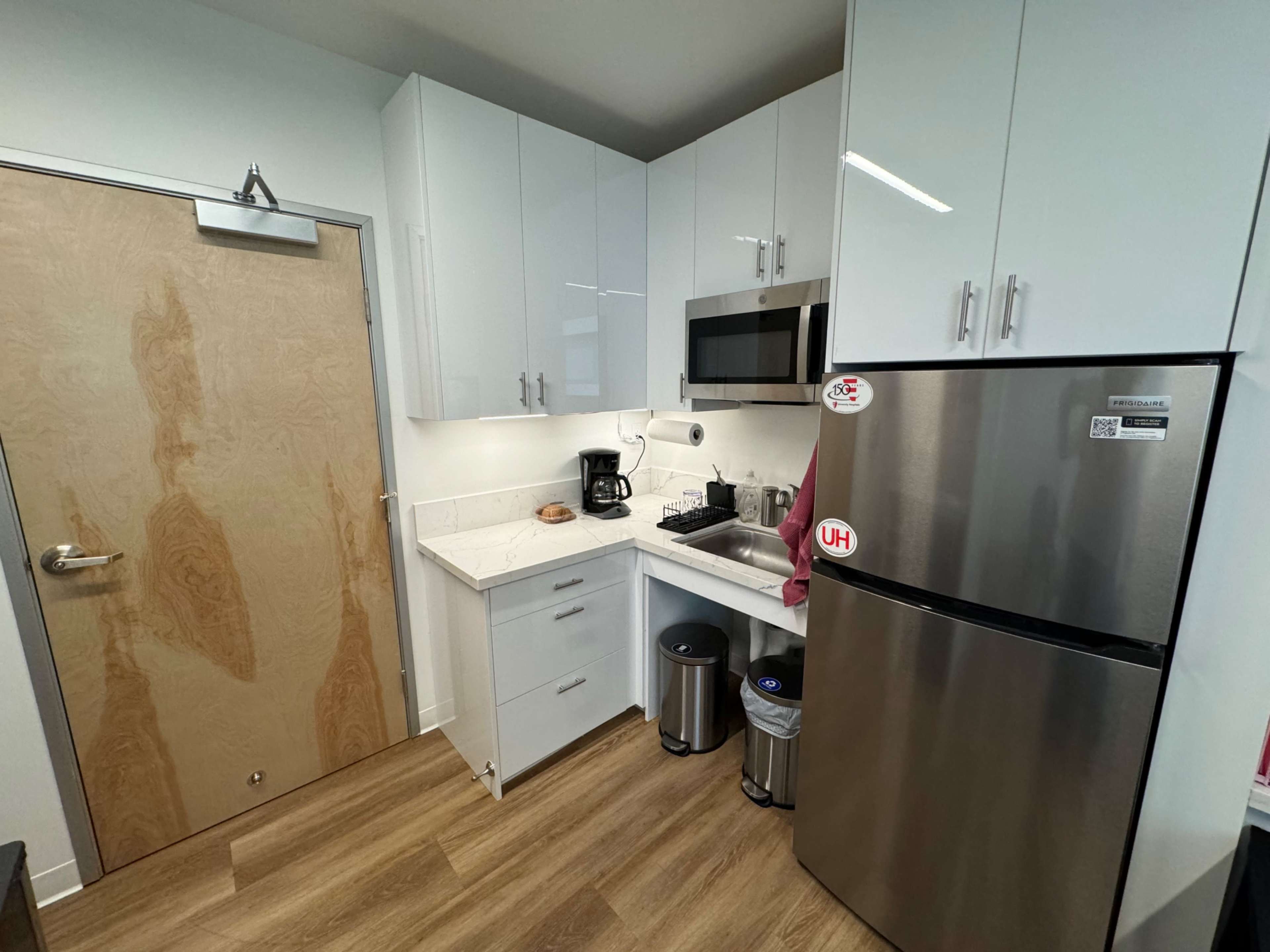 A small kitchen featuring white cabinets, a stainless steel refrigerator, a microwave, and a coffee maker on the countertop.