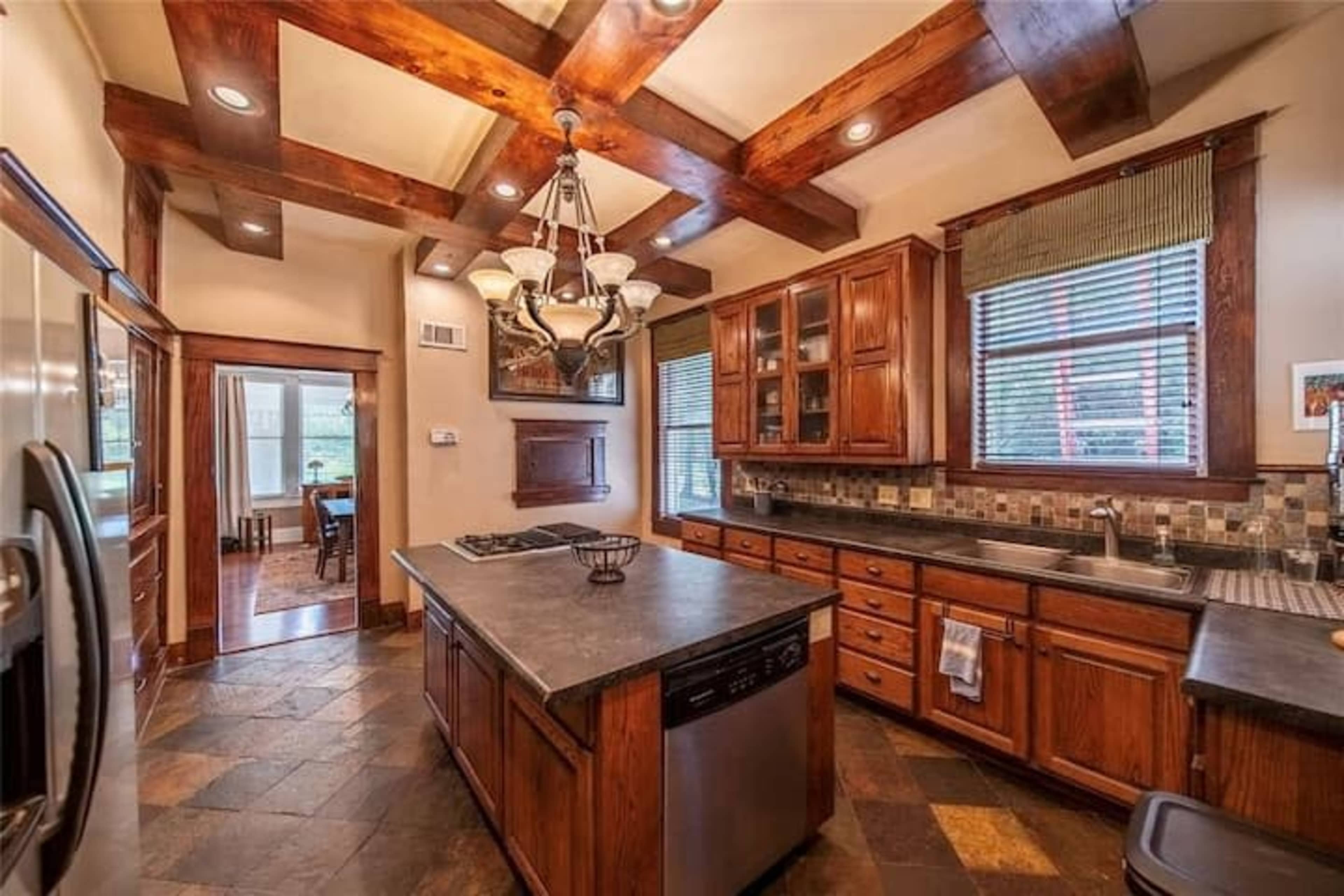 A spacious kitchen featuring wooden cabinets, a large island, and a mix of stone and tile flooring.