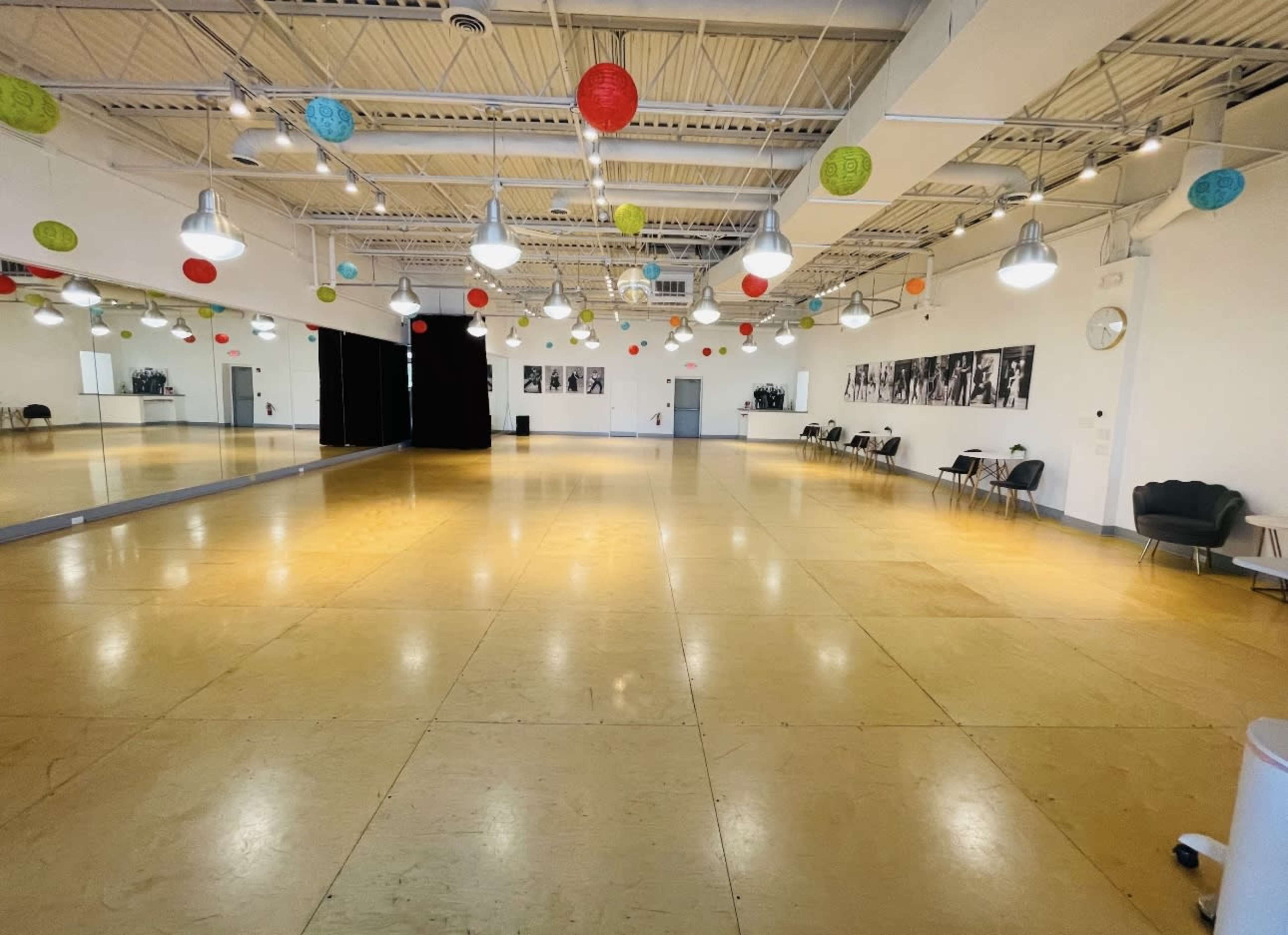 The image shows a spacious dance studio with a polished floor, mirrors on one wall, and colorful paper lanterns hanging from the ceiling.