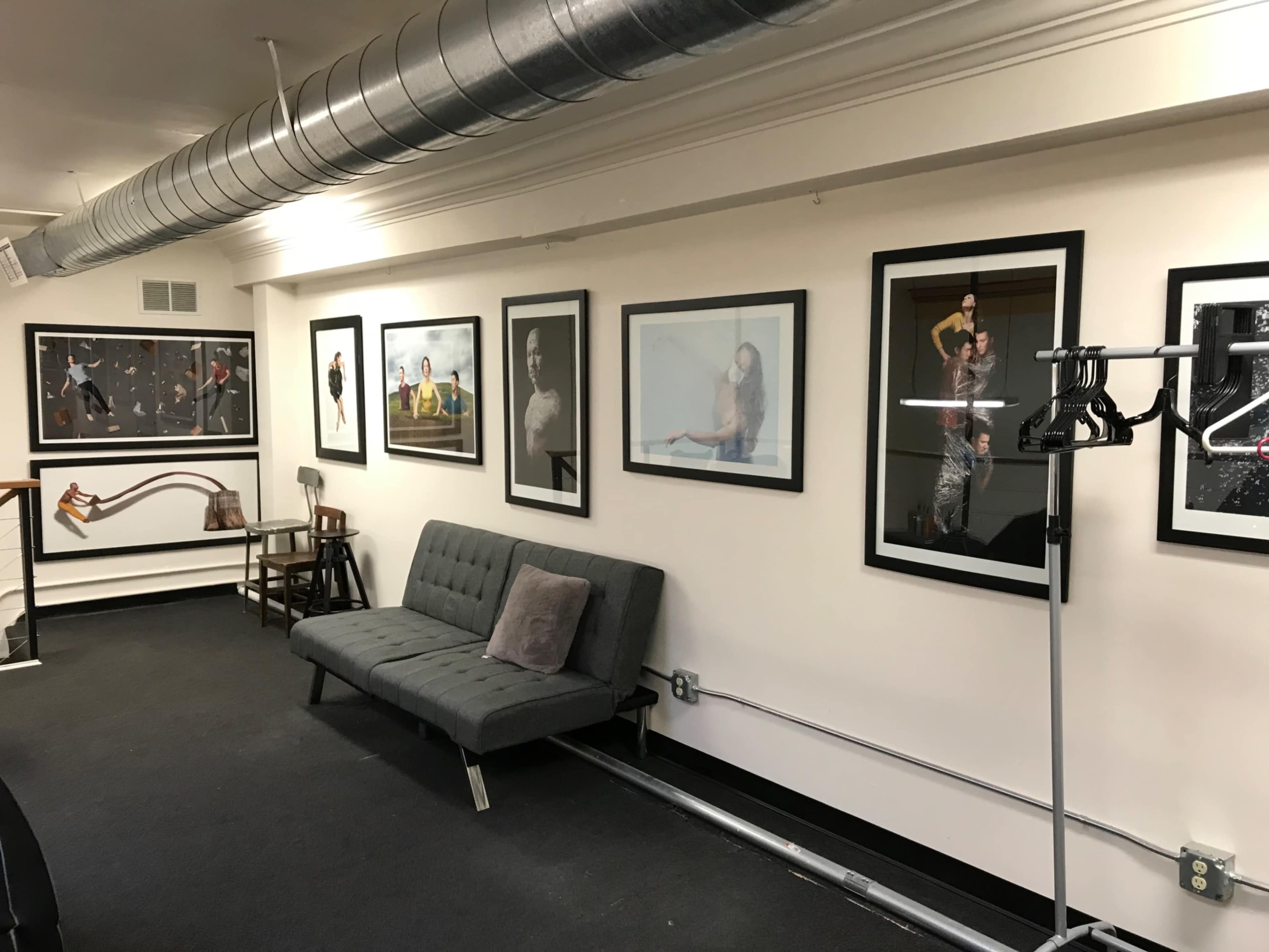 A waiting area featuring a gray sofa, several framed artworks on the wall, and a clothing rack on the right.