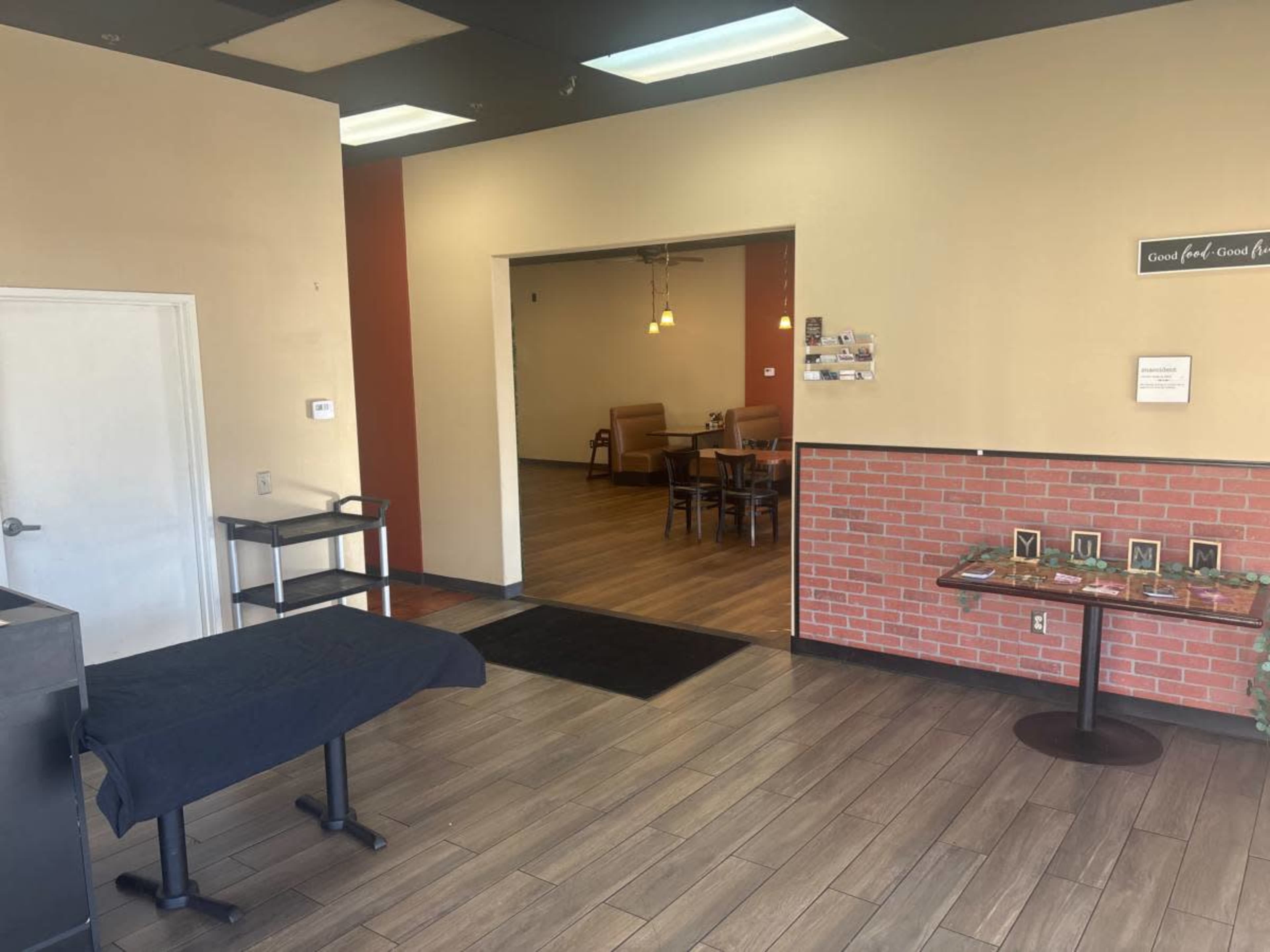 The image shows the entrance of a restaurant with a reception area in the foreground and a dining area visible through an open doorway.