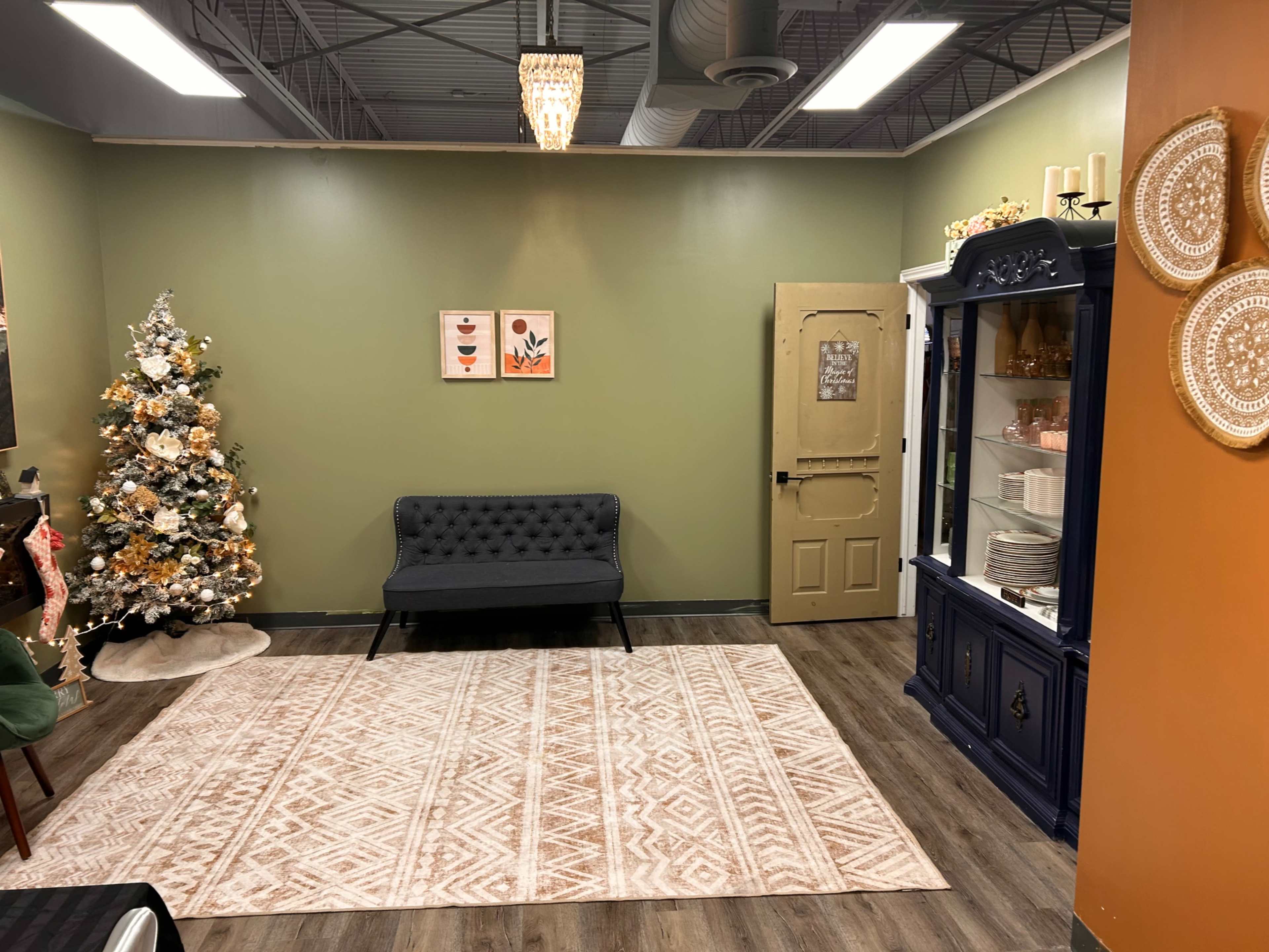The room features a decorated Christmas tree, a grey sofa, a cabinet, and a large area rug on the floor.