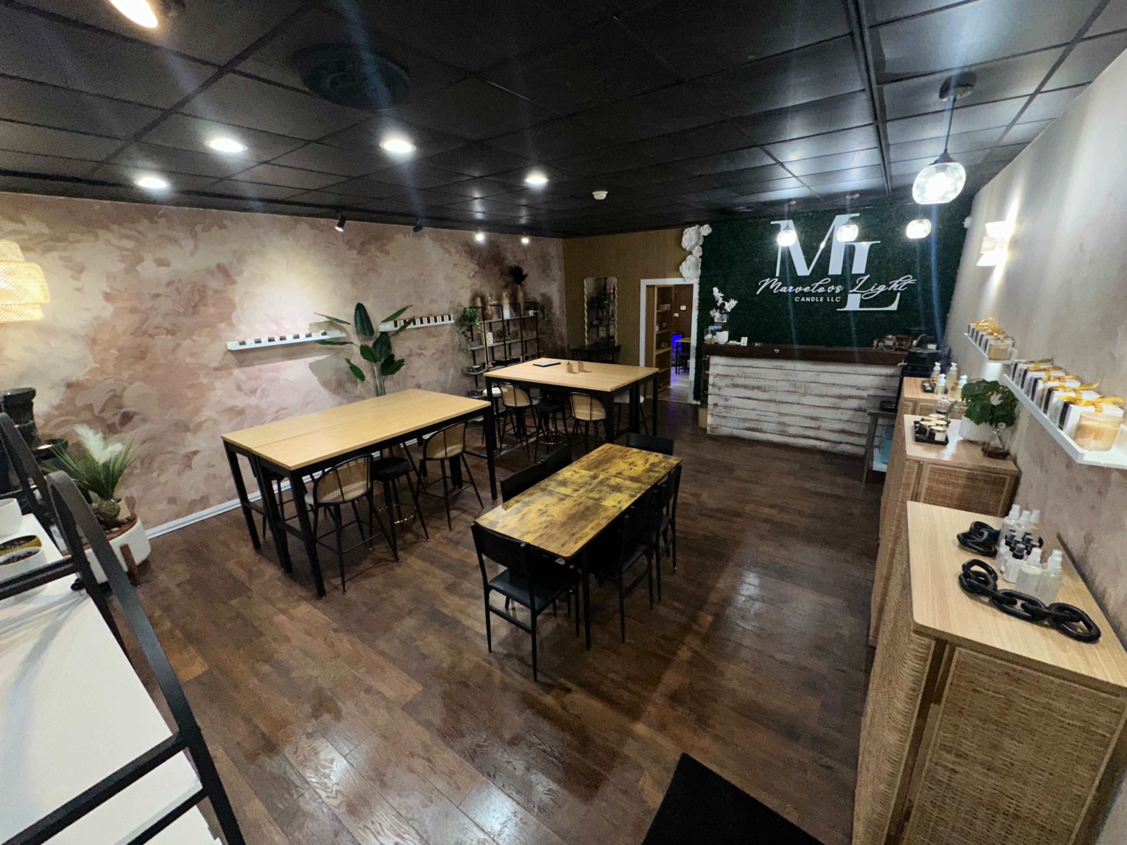The image shows a spacious, modern café interior with wooden tables, a plant, and a stylish counter featuring decorative items and a logo on the wall.