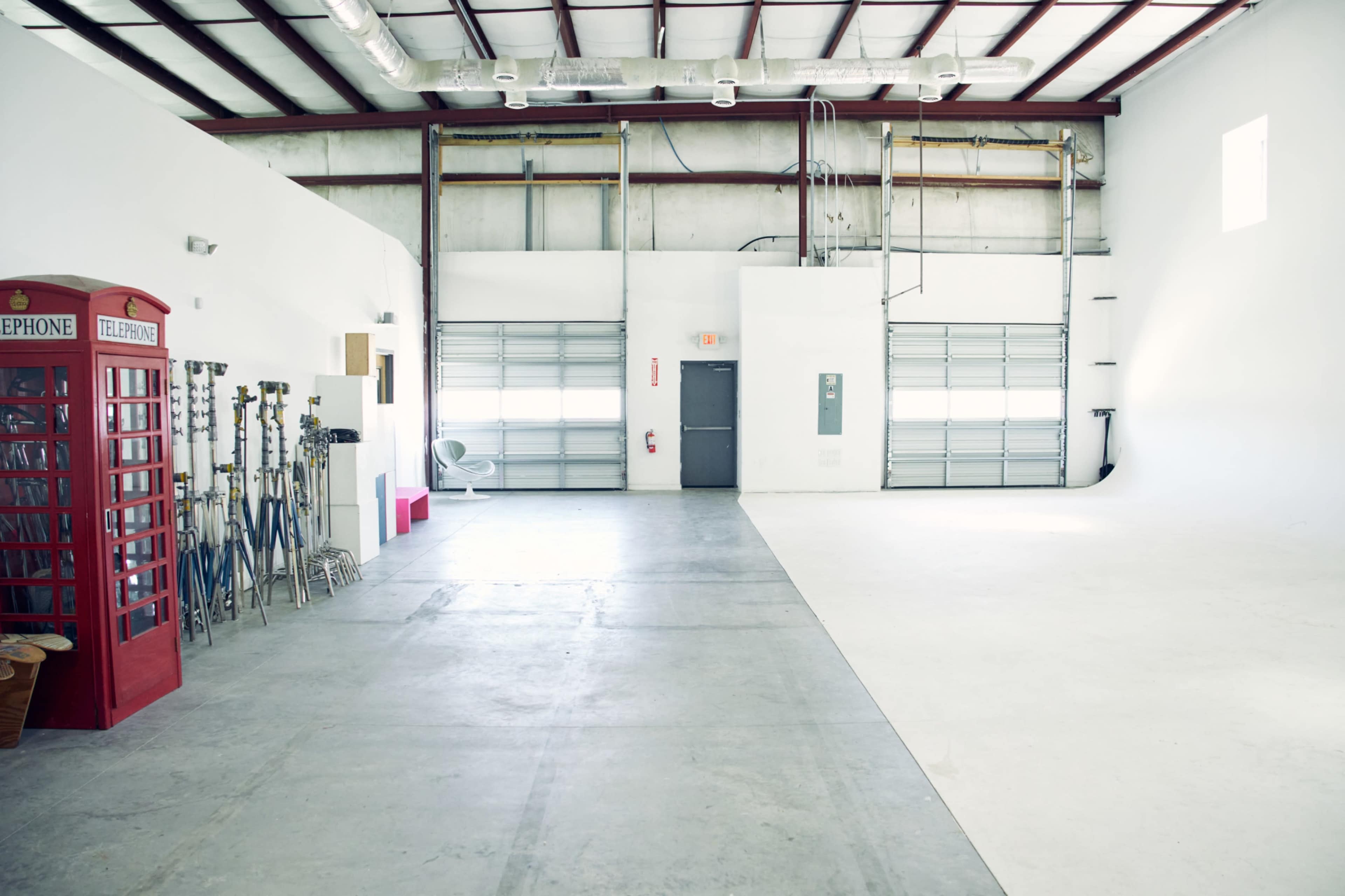 The image shows a spacious, uncluttered warehouse with a red phone booth on one side and various equipment stands lined up against the wall.