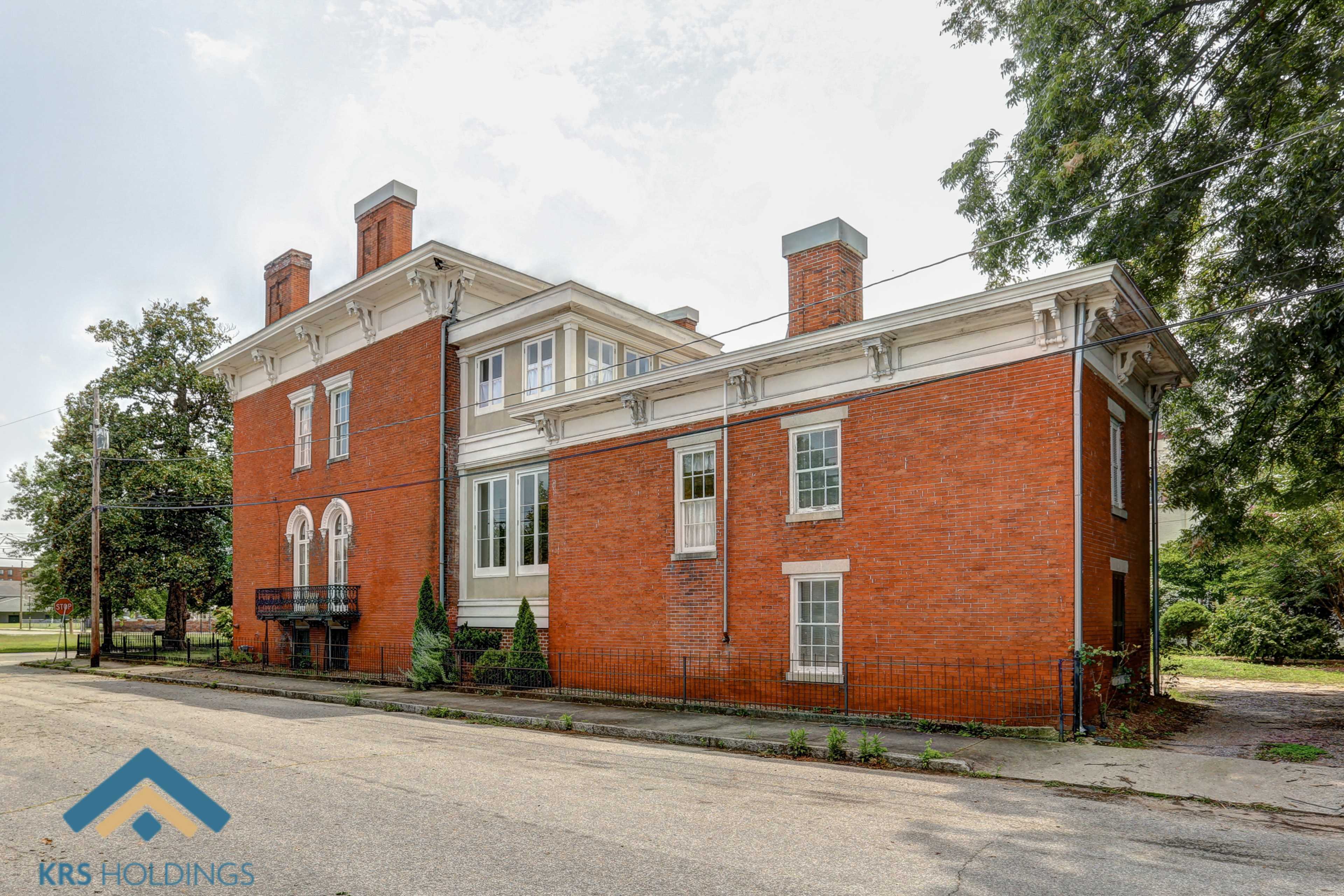 A two-story brick building with white trim and several windows, situated on a street lined with trees.