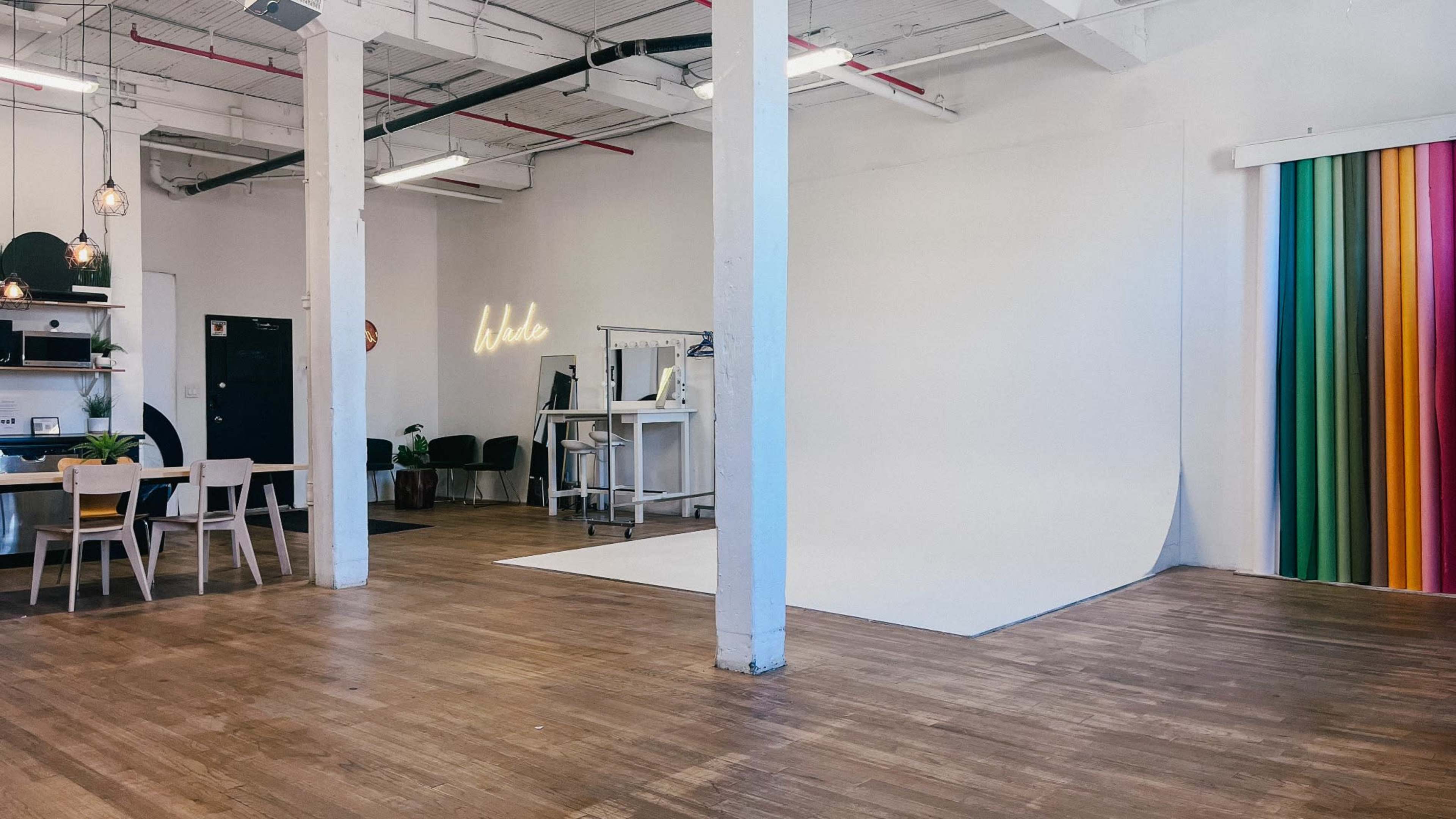The image shows a spacious studio featuring a white backdrop, a wooden floor, modern furniture, and colorful drapery against one wall.
