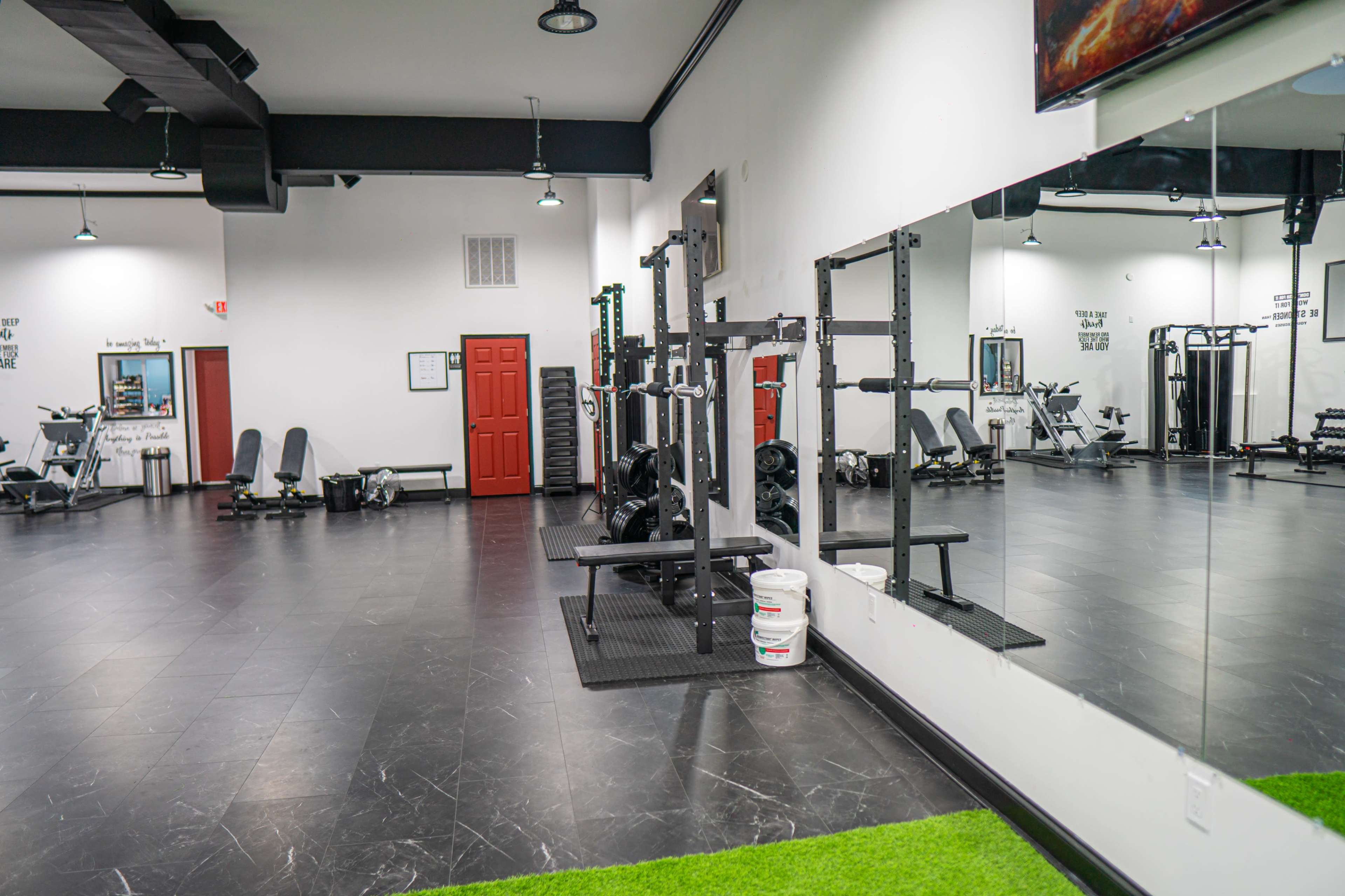 A modern gym interior featuring weightlifting equipment and exercise machines arranged around a mirrored wall.