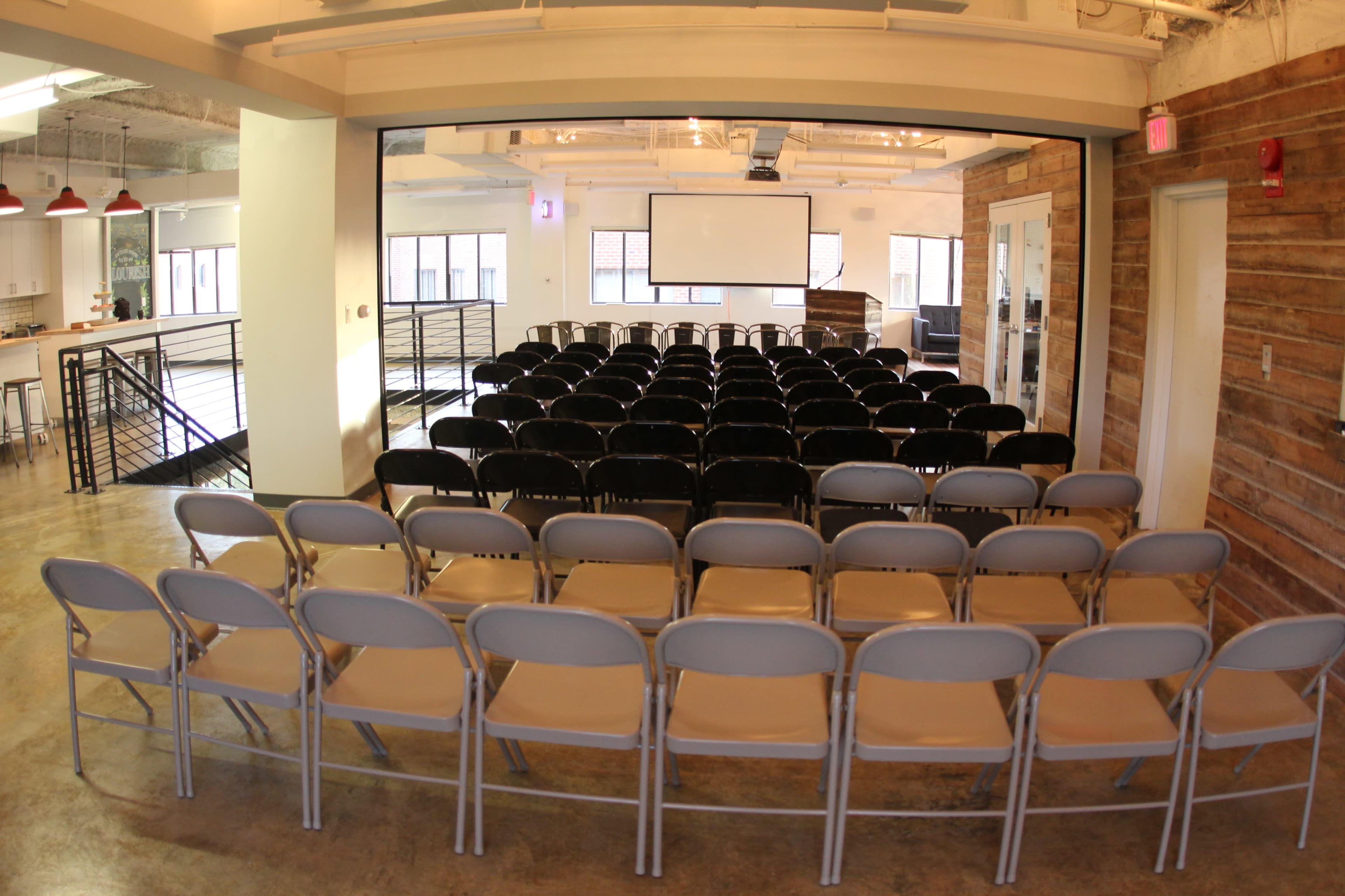 A row of folding chairs arranged facing a large screen in a spacious, well-lit room.