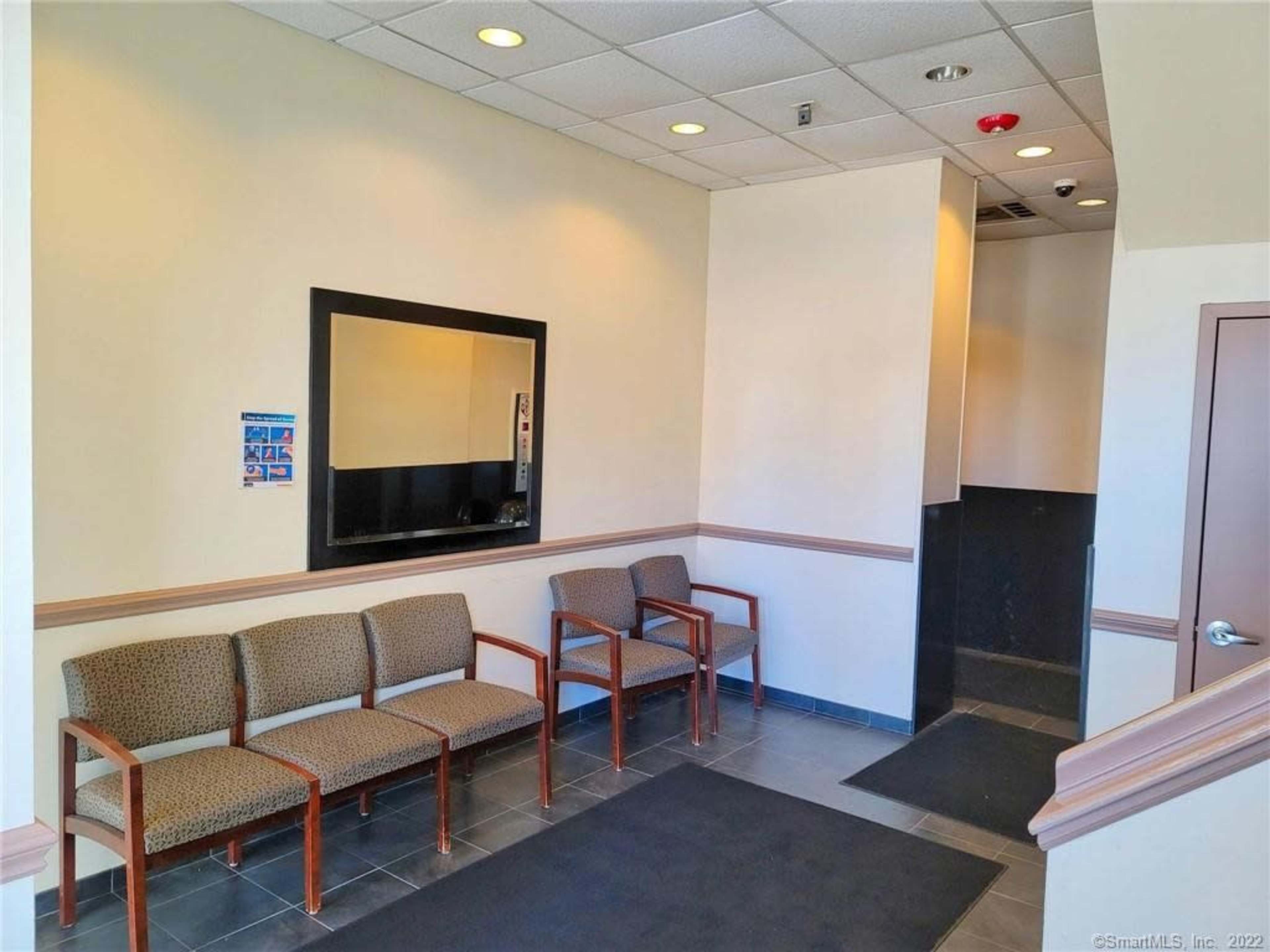 A waiting area with three upholstered chairs and a wall-mounted mirror in a well-lit space.