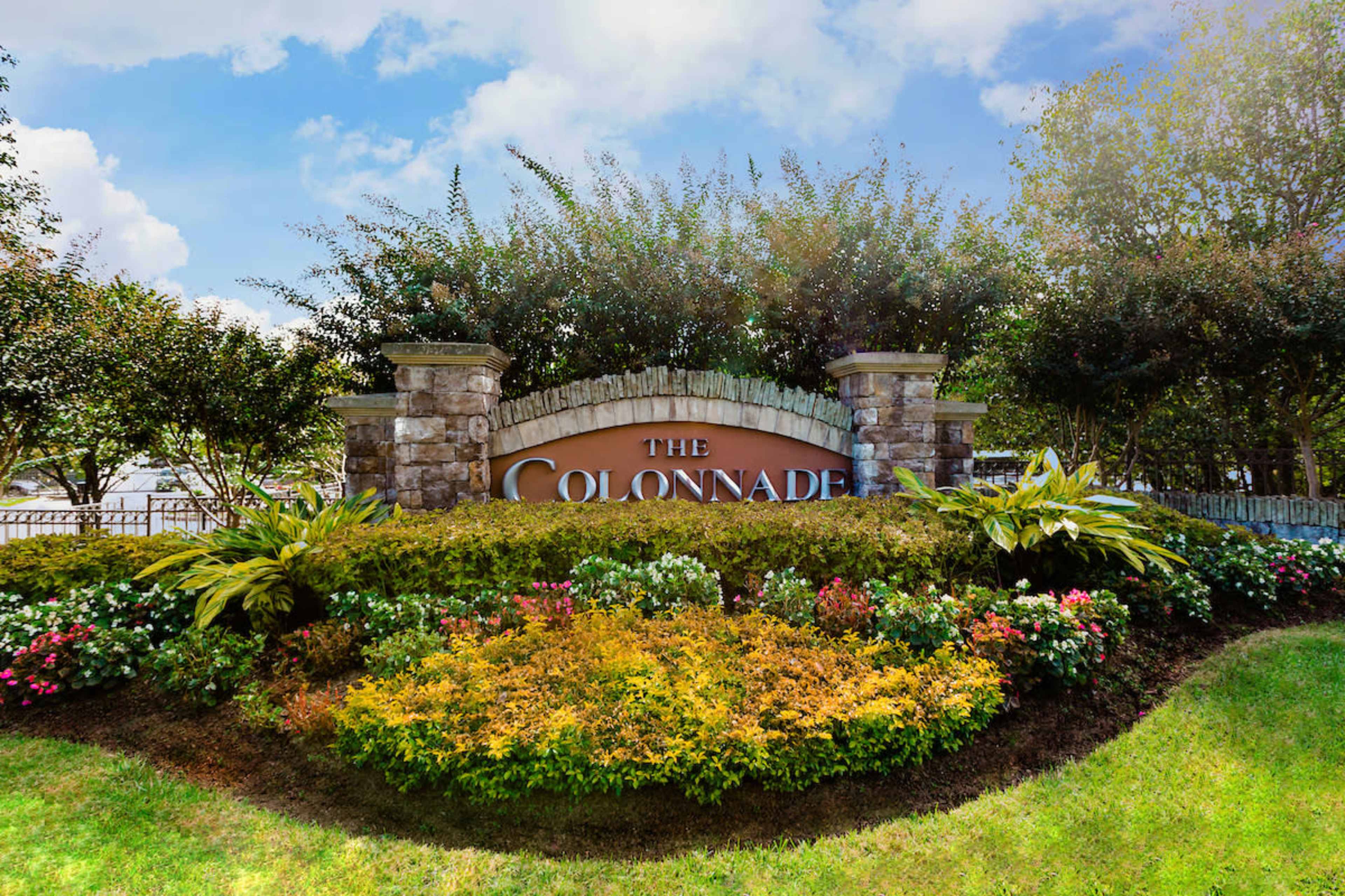 A large sign that reads "The Colonnade," surrounded by well-maintained landscaping with various plants and flowers.