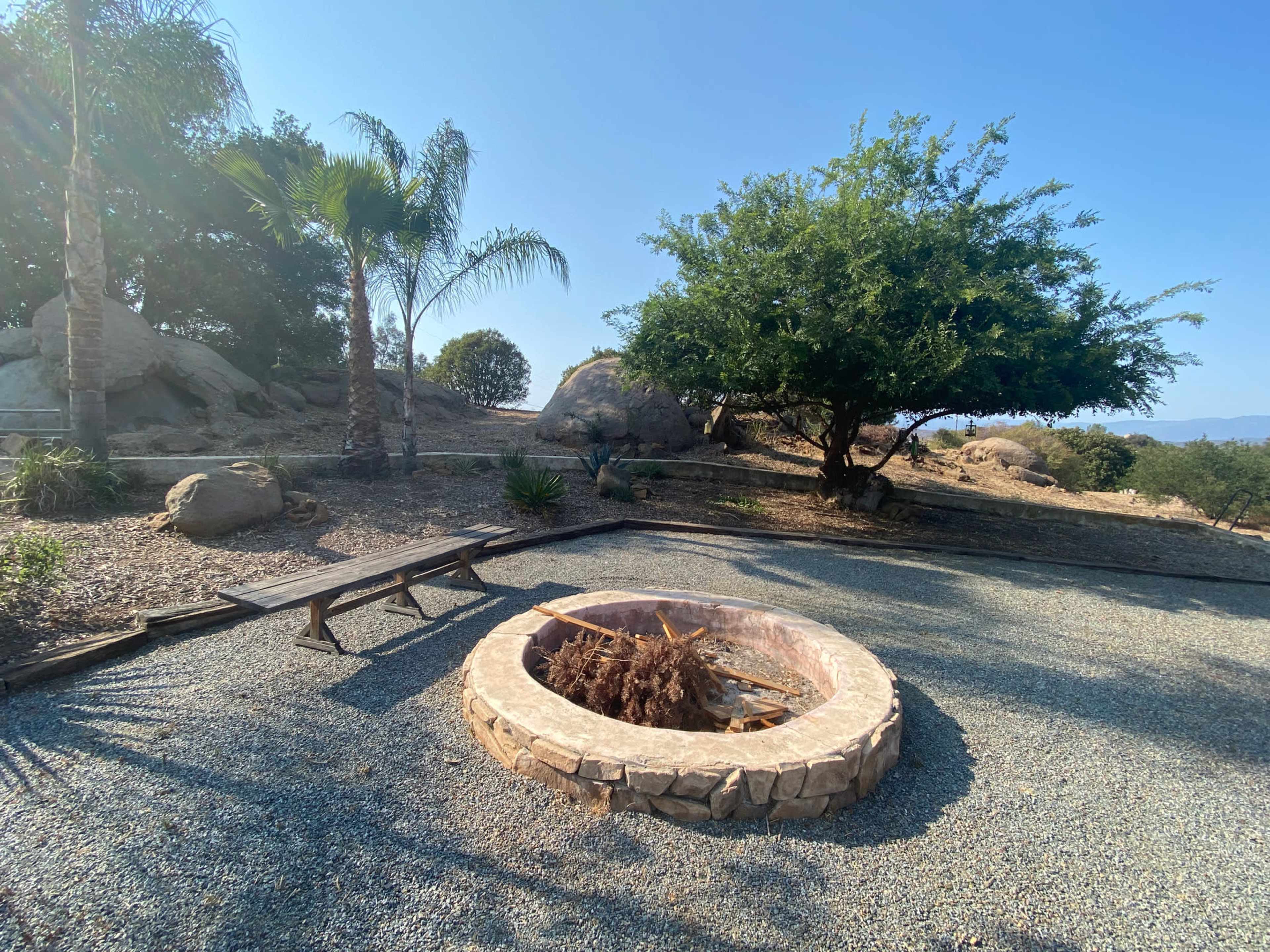 A stone fire pit surrounded by gravel and palm trees in a scenic outdoor setting.