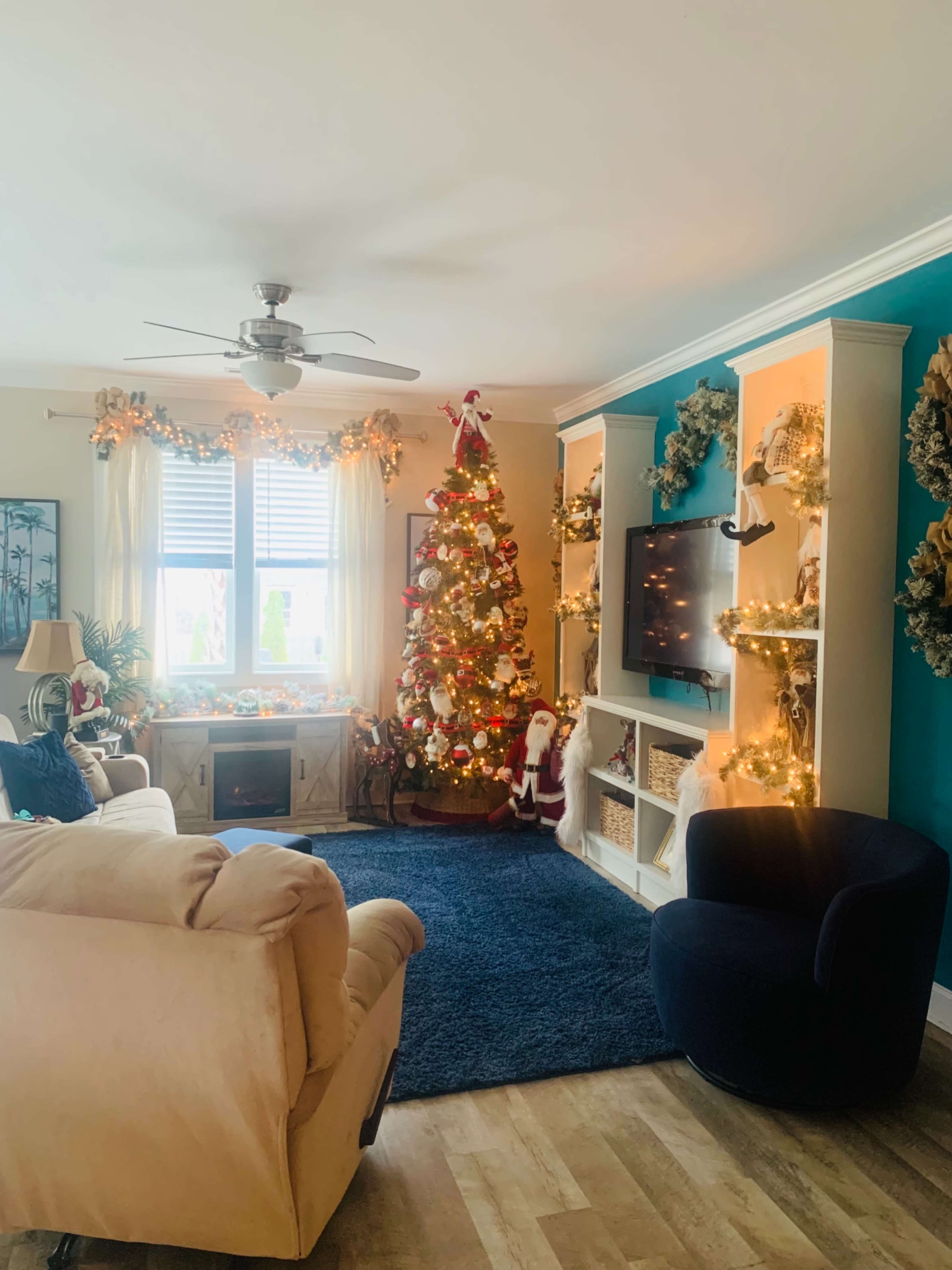 The living room features a decorated Christmas tree, a cozy armchair, and a wall-mounted television with festive decorations.