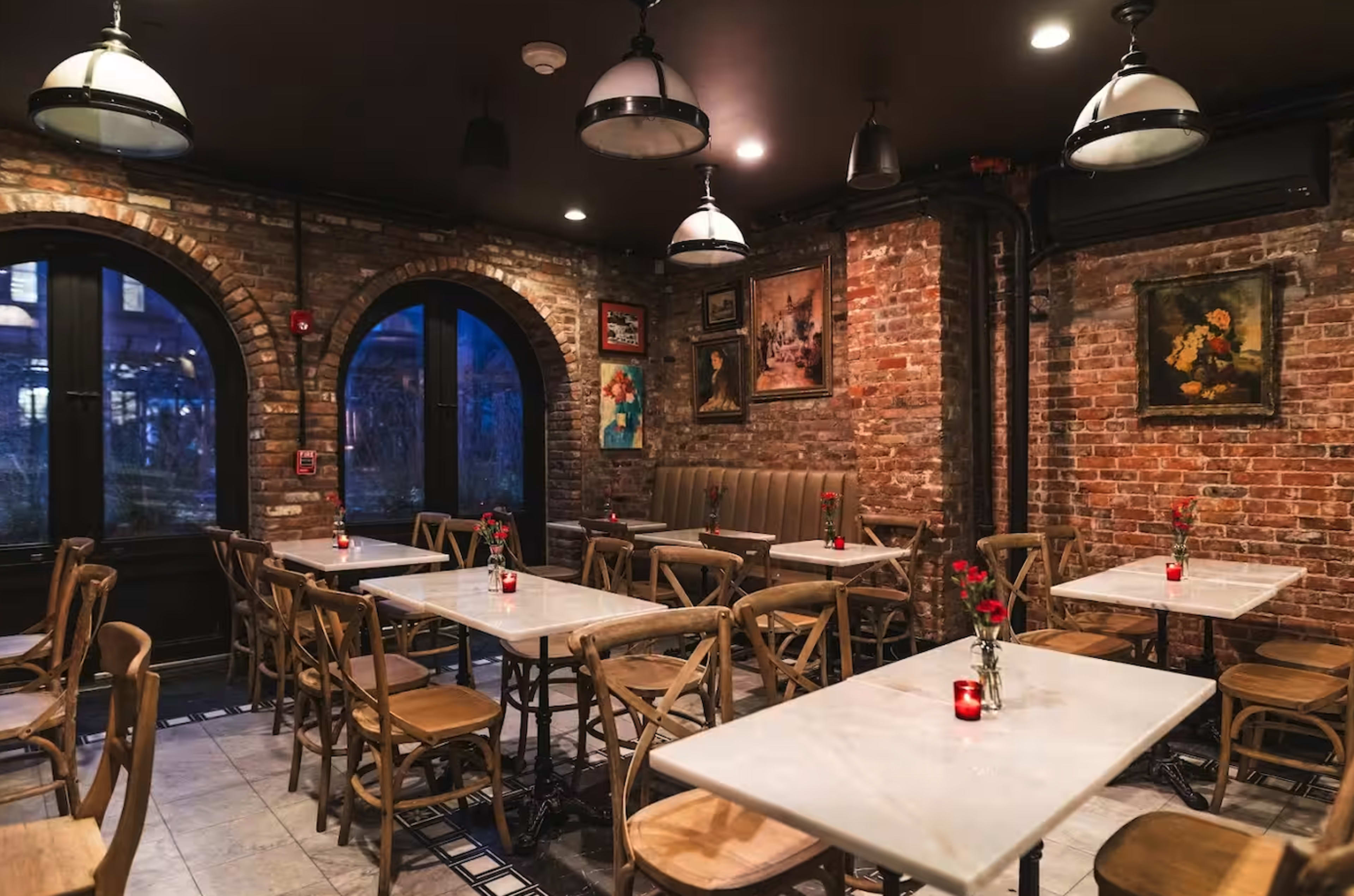 The image shows a cozy restaurant interior with exposed brick walls, marble-topped tables, and wooden chairs, illuminated by soft lighting.