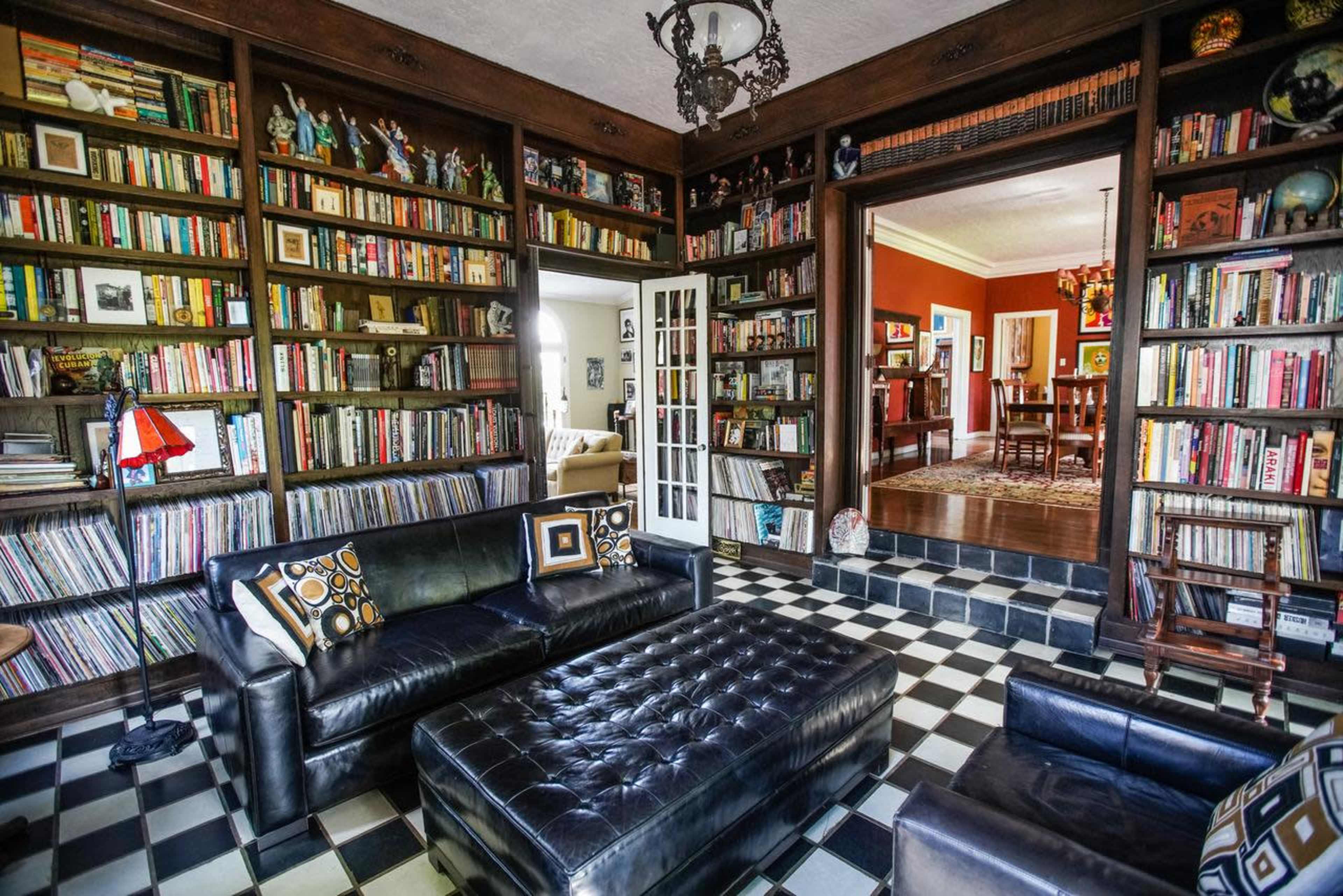 A cozy living room features black and white tiled flooring, extensive bookshelves filled with books, and a black leather sofa with decorative pillows.