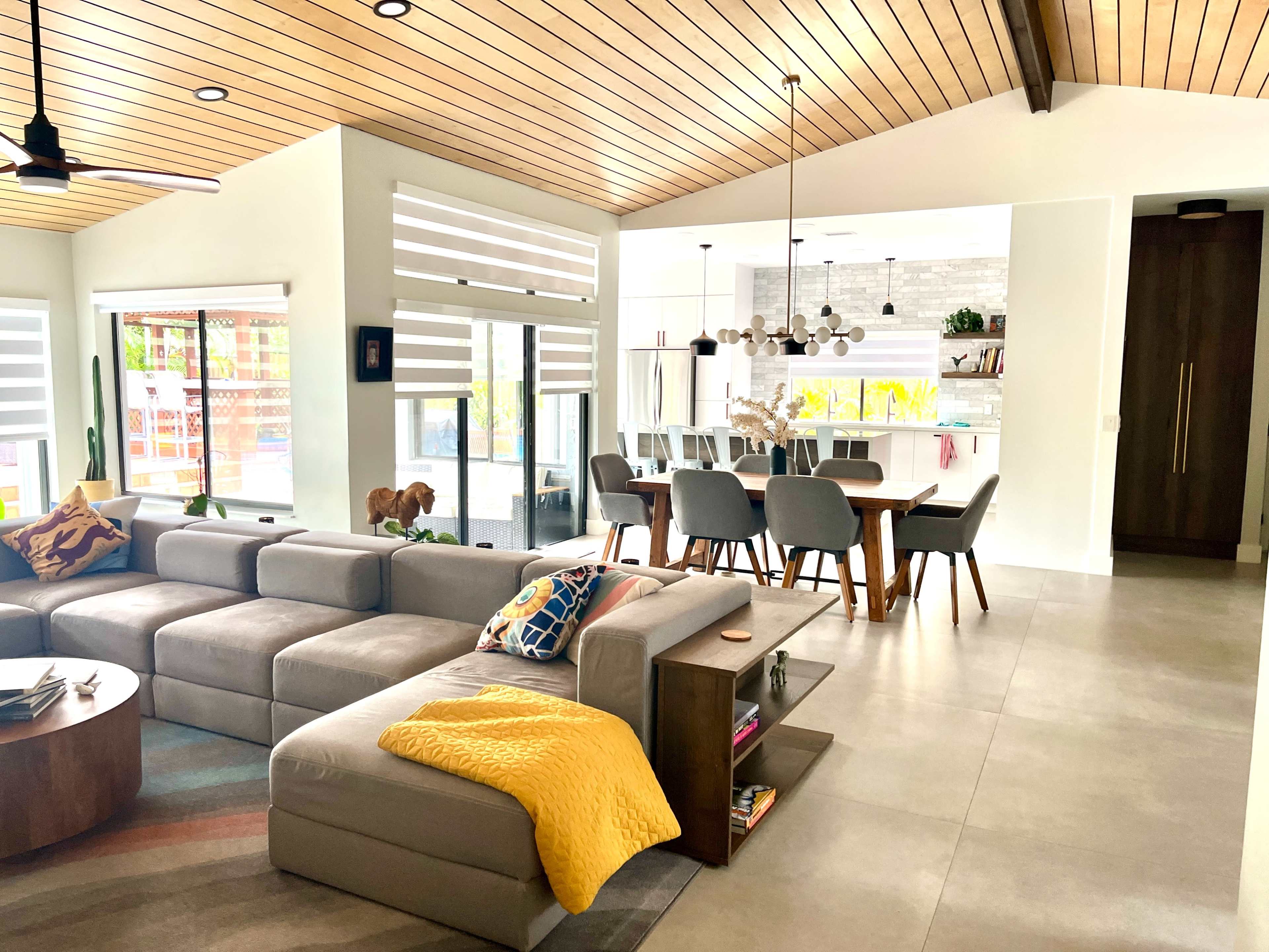 A modern living space featuring a sectional sofa, dining area, and a kitchen with contemporary furnishings and large windows.