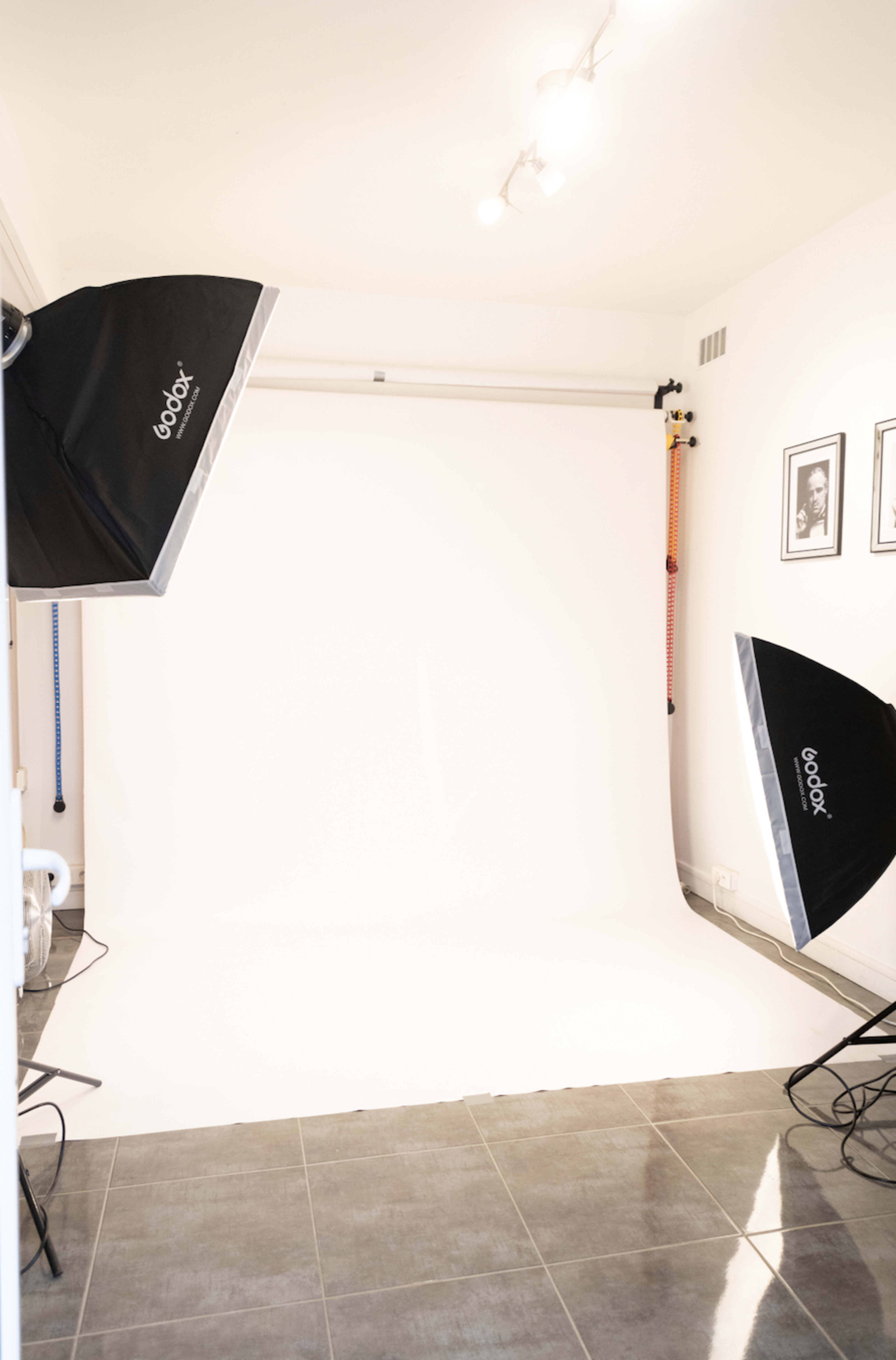 A photography studio with a plain white backdrop and two softbox lighting setups on each side.