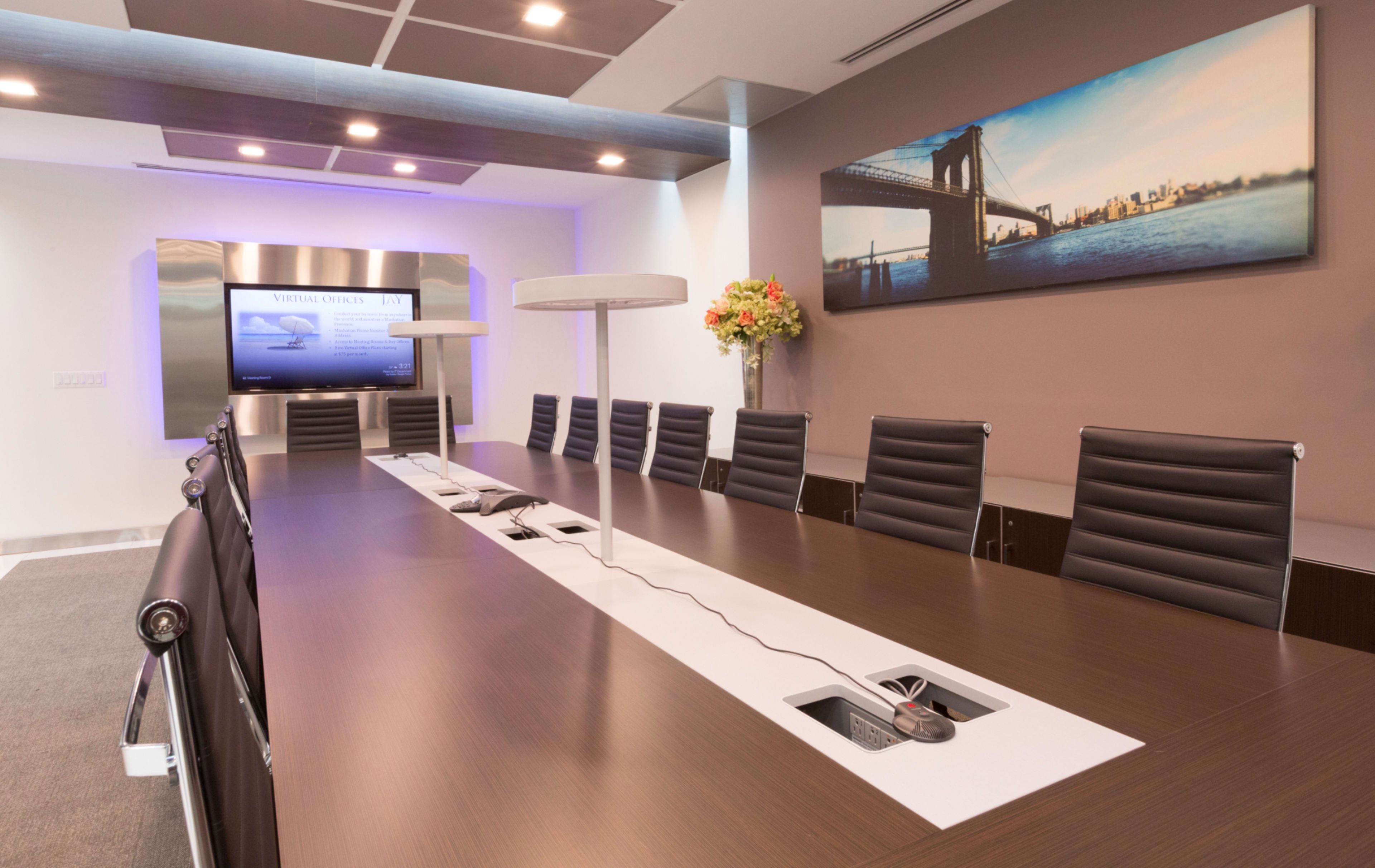 A modern conference room features a long table with black leather chairs, equipped with multimedia displays and a decorative wall featuring a city skyline.