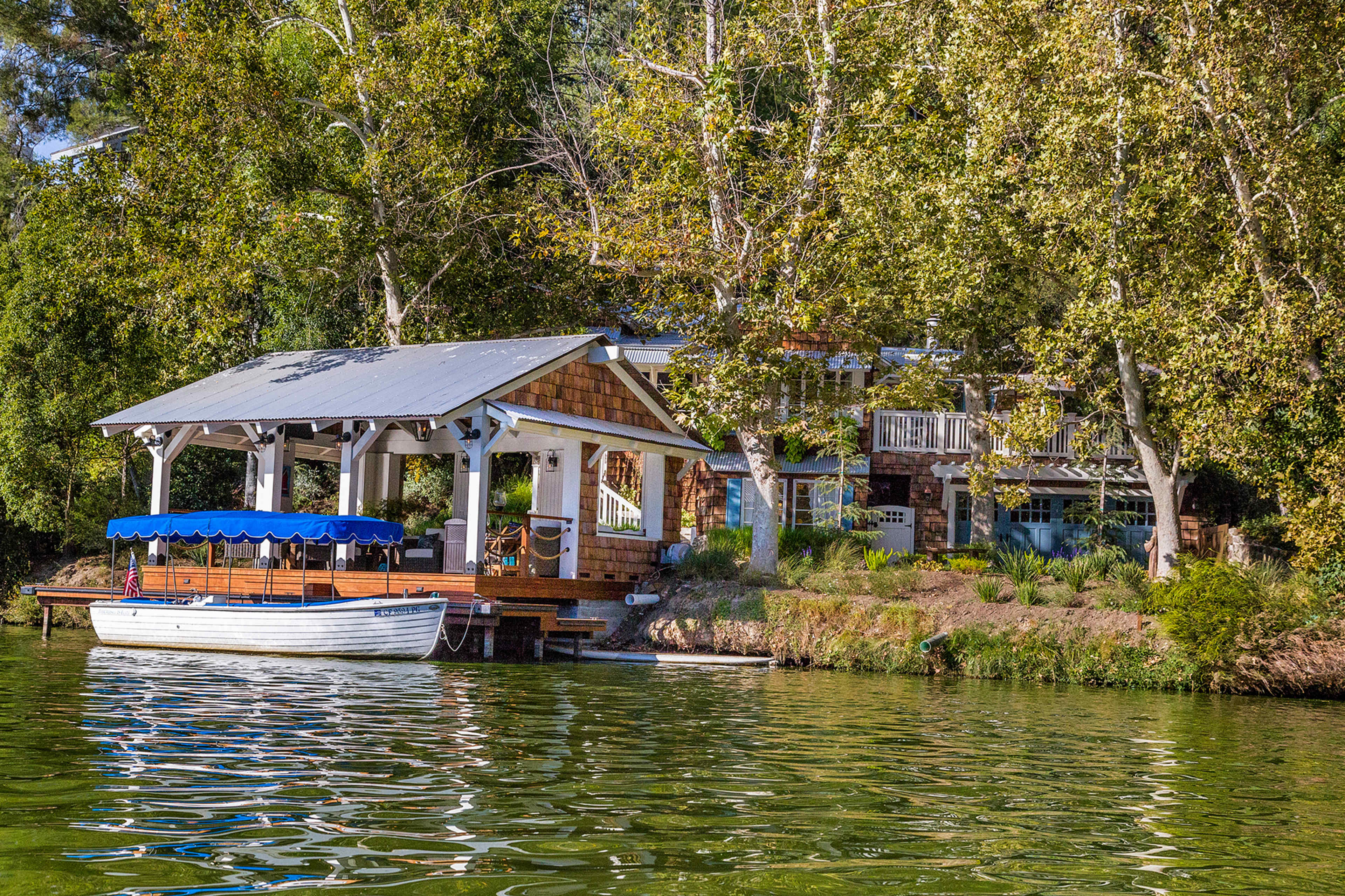 A wooden boat is tied to a dock beside a house surrounded by trees near a calm lake.