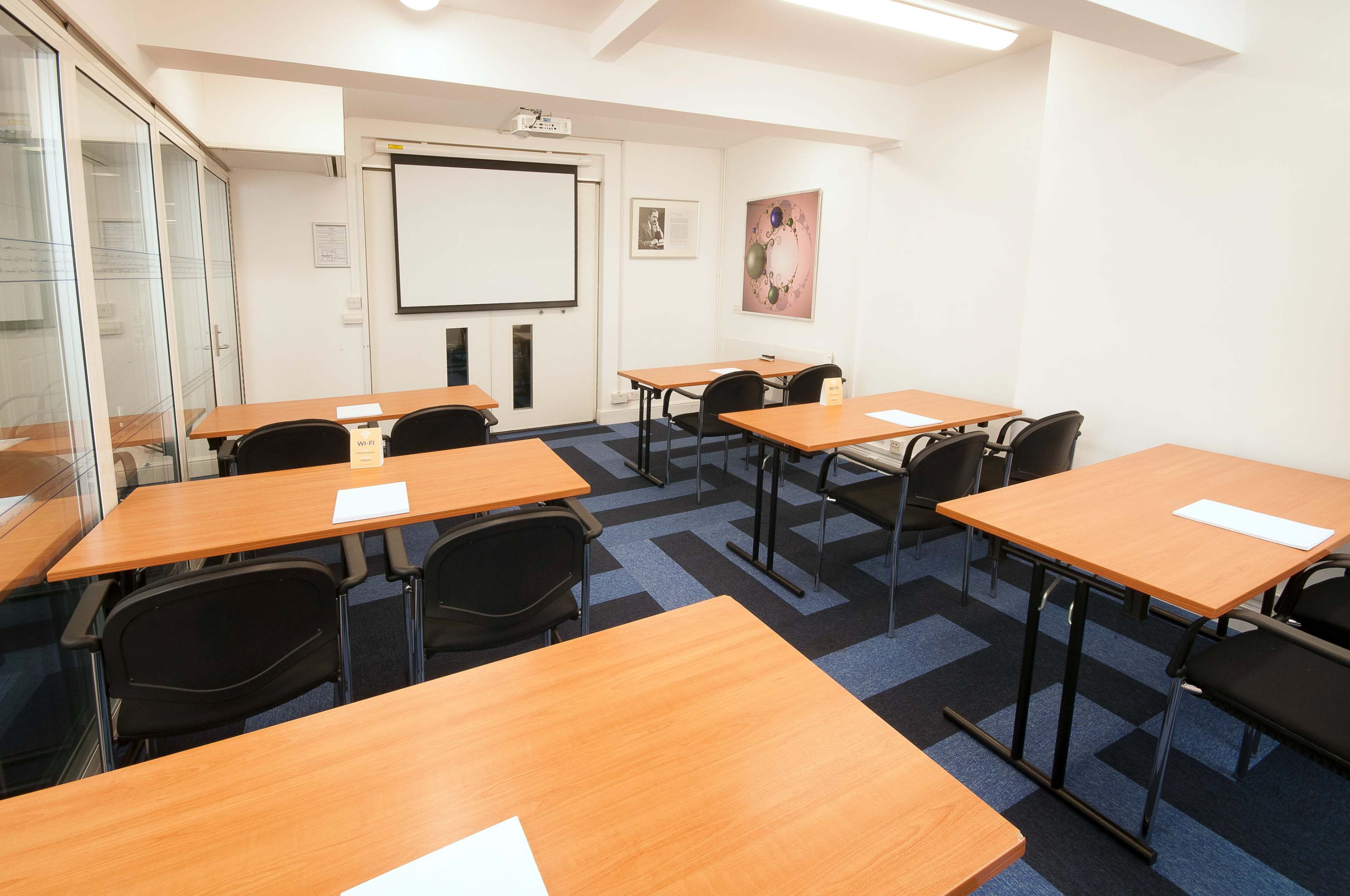 A training room is set up with several wooden tables and chairs, facing a projection screen on the wall.