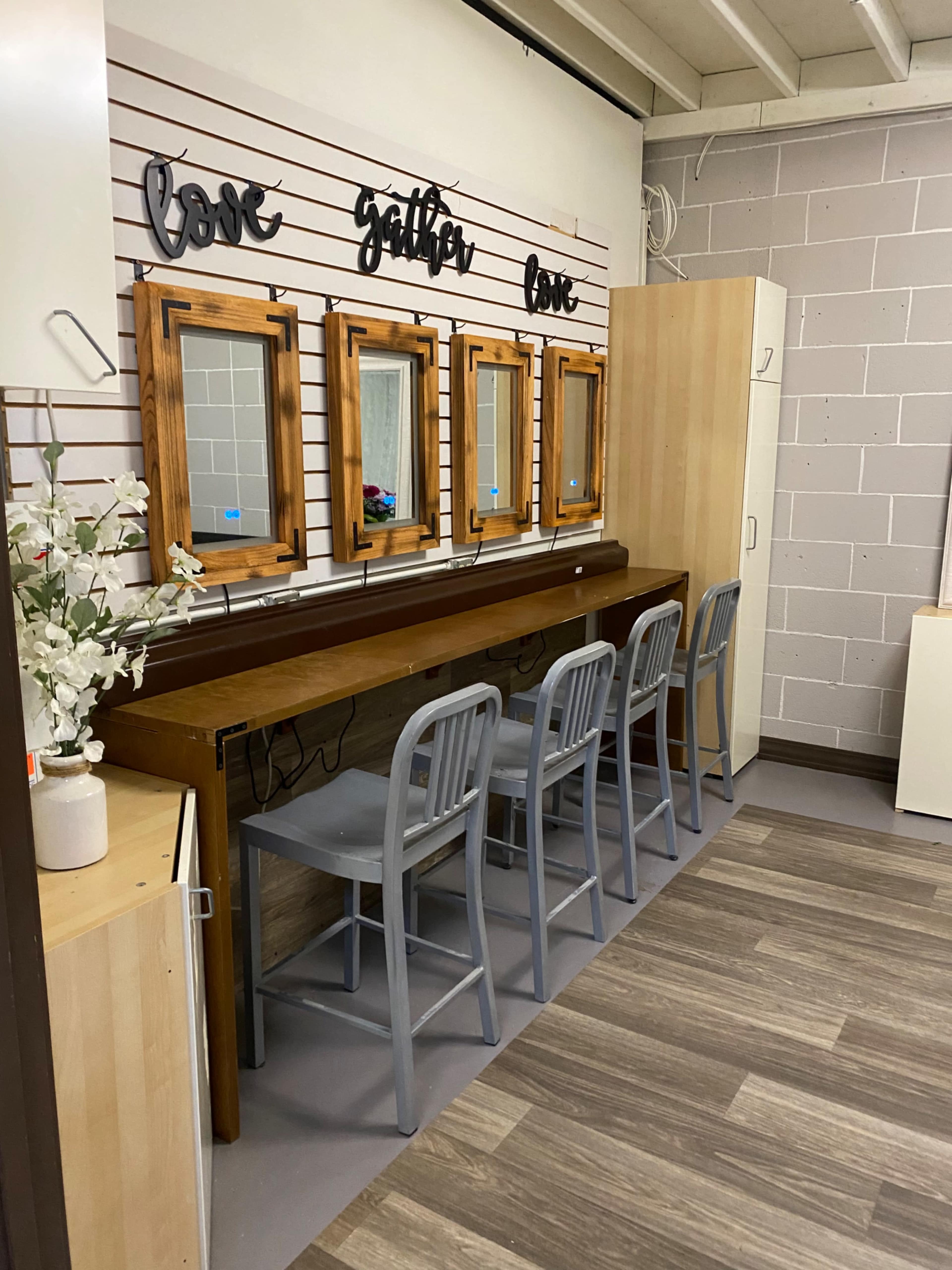 A room with a long wooden table and four gray chairs in front of three framed mirrors mounted on a wall with decorative text above.