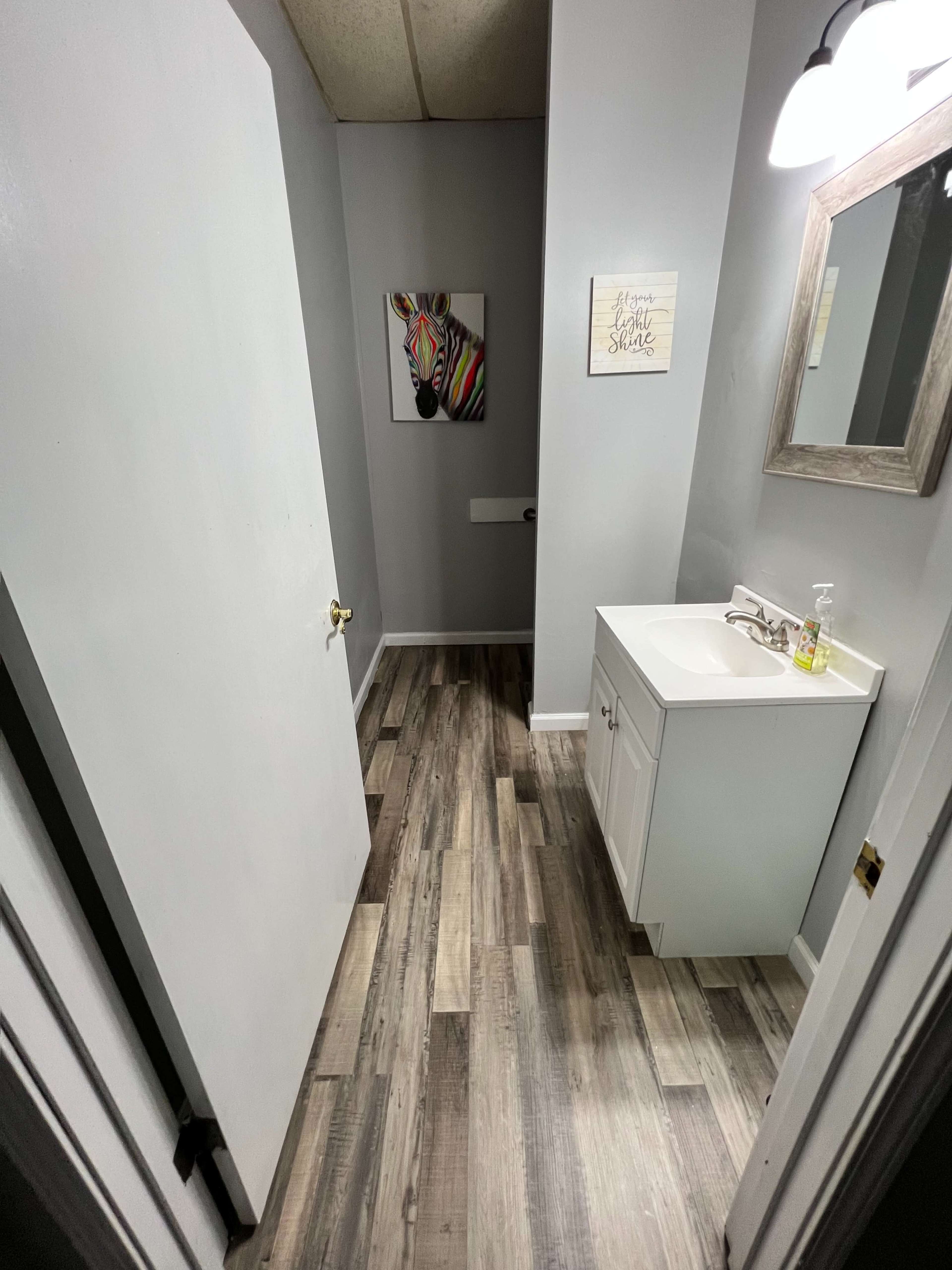 A modern bathroom with gray walls, a white vanity, and a piece of artwork featuring a colorful zebra on the wall.