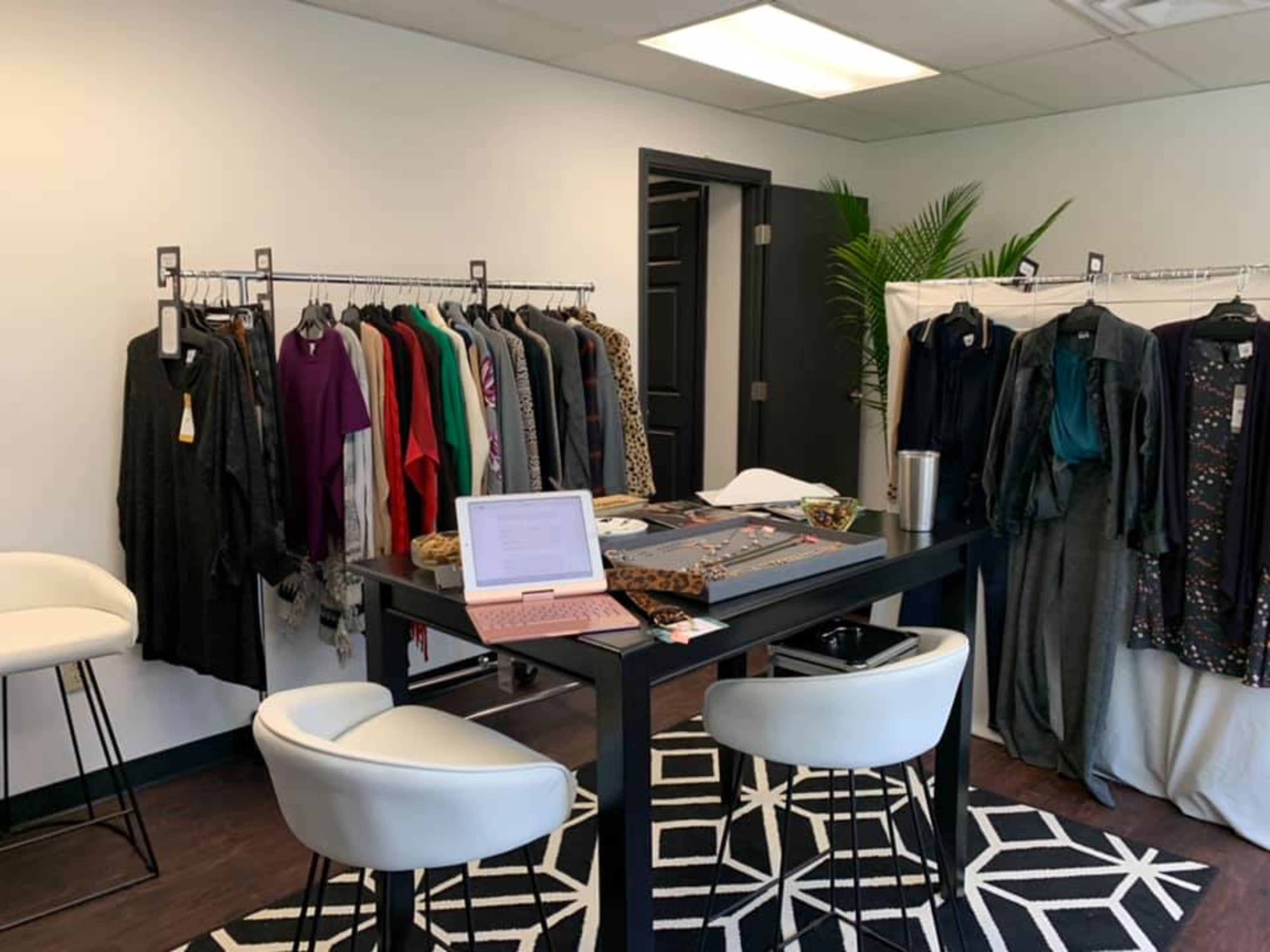A clothing showroom featuring racks of apparel, a black table with a laptop, and seating arranged in a modern setting.
