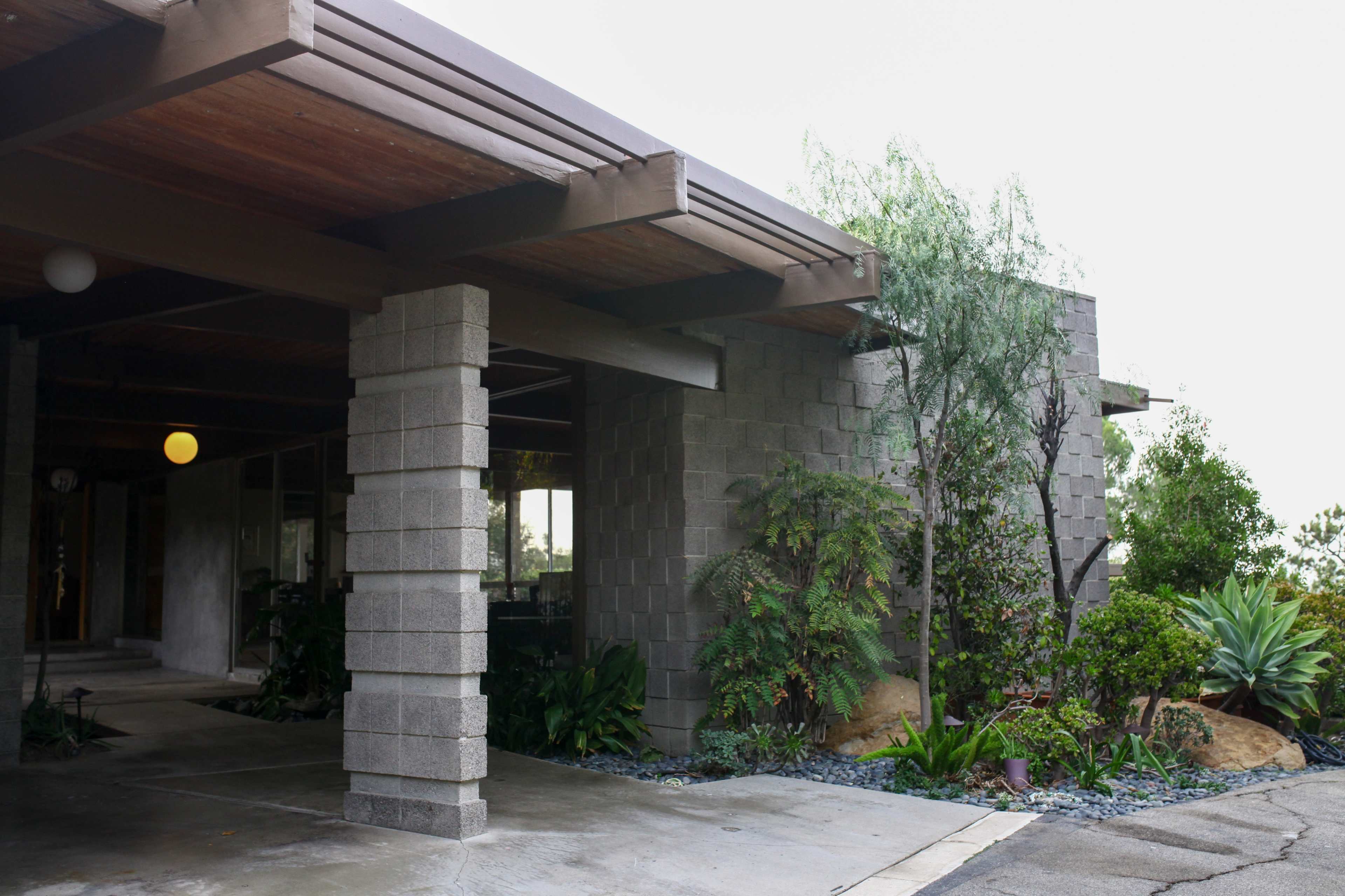 A modern architectural house with a concrete block exterior, surrounded by various plants and landscaping.