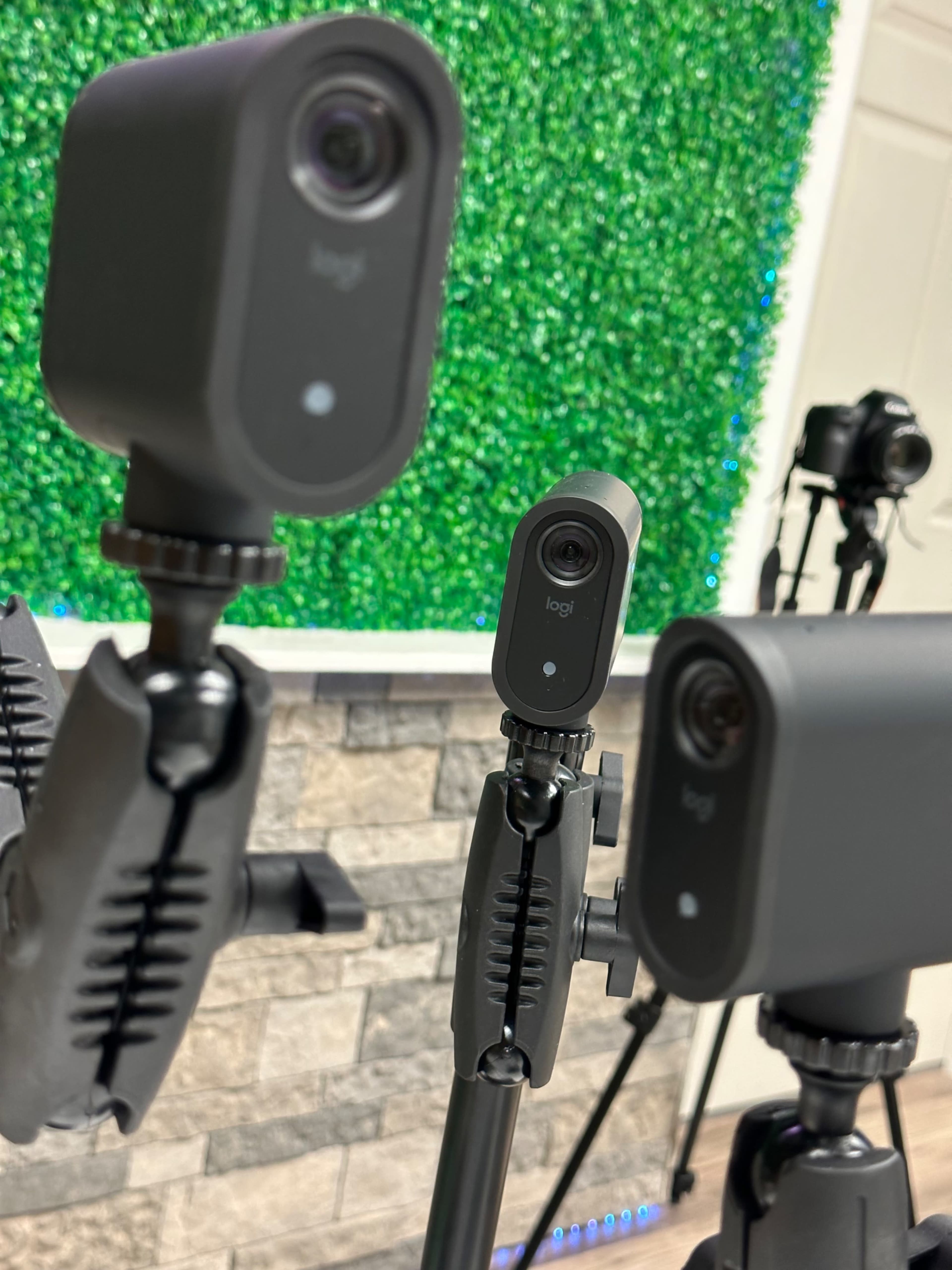 The image features a close-up of multiple Logitech cameras mounted on adjustable tripods against a green decorative background.